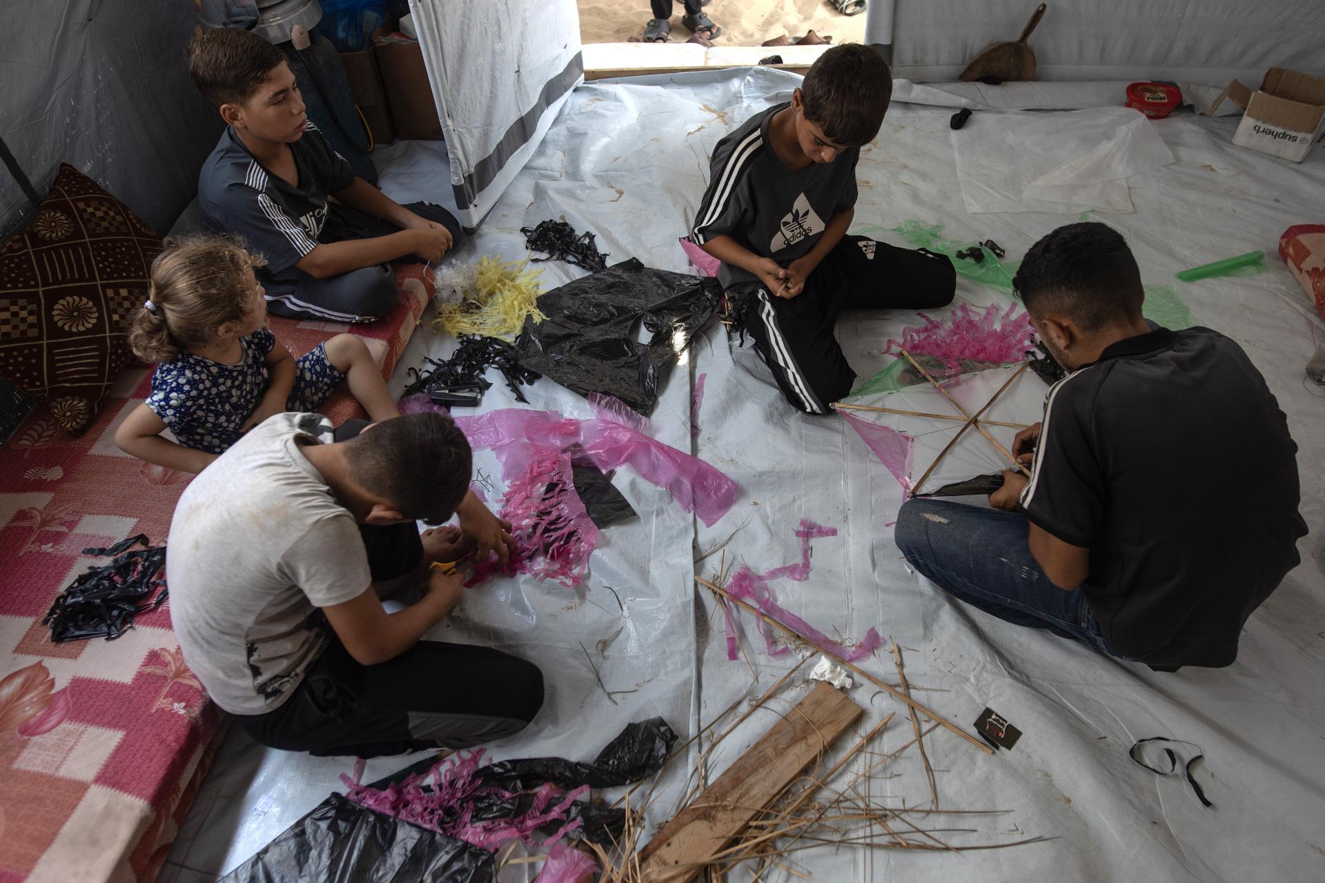 Khan Younis (-), 27/08/2026.- Palestinian children craft kites at al-Mawasi camp, near Khan Younis, southern Gaza Strip, 27 August 2026. Without safe places to play, displaced Palestinian children make kites from basic materials to cope with displacement and the heat inside their tents, and find a moment of relief. However, recent warnings from the Israeli military against kite-flying have turned a harmless children’s game into another source of fear and anxiety inside the displacement camps. EFE/EPA/HAITHAM IMAD

