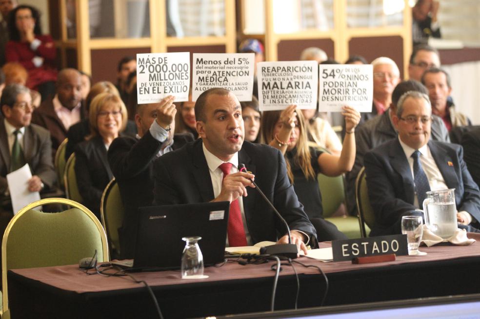 El representante del Estado Venezolano, Larry Devoe, responde a miembros de la Comisión Interamericana de Derechos Humanos (CIDH), mientras asistentes a la audiencia pública "Derecho a la alimentación y a la salud de Venezuela", protestan contra el Gobierno de Caracas en febrero de 2018.