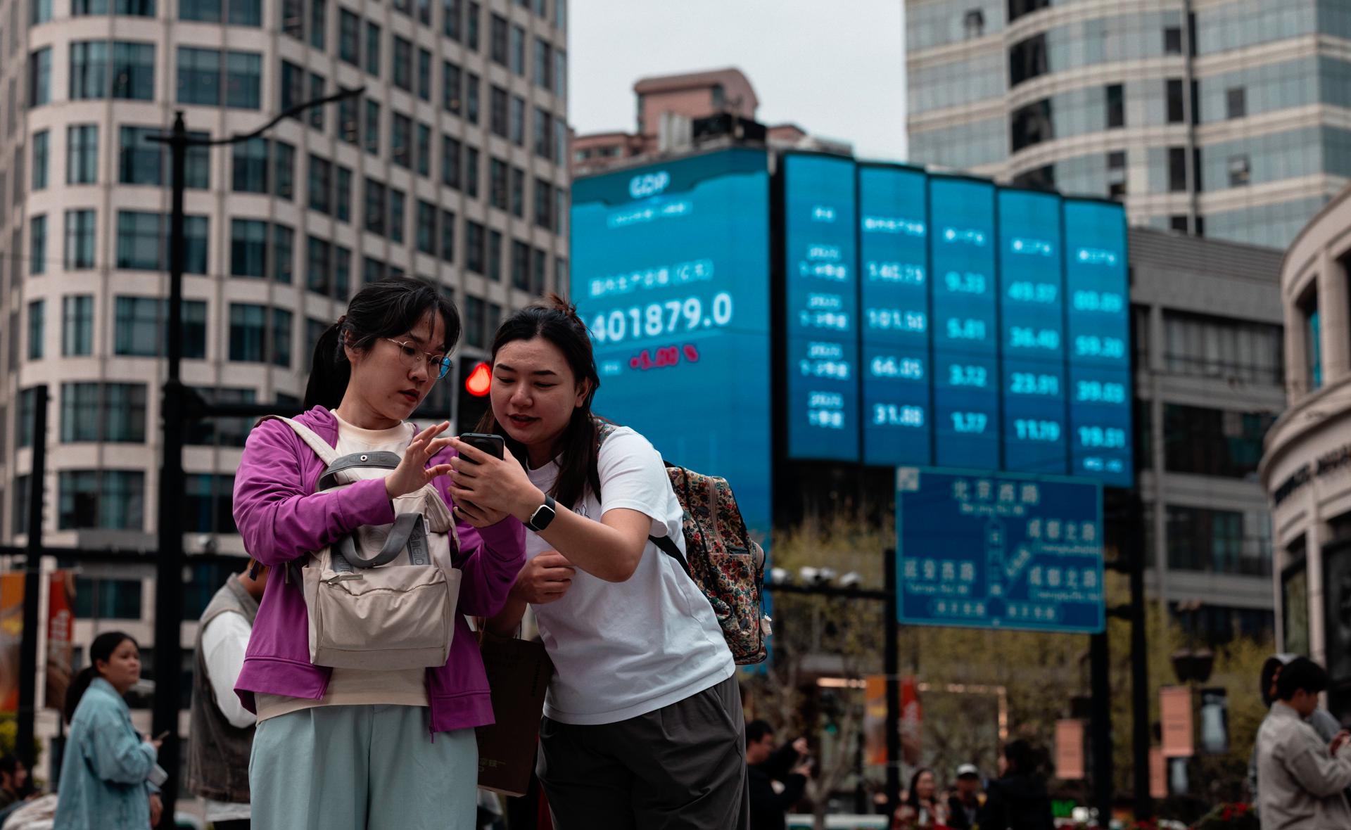 Shanghai (China), 08/04/2026.- People stand beneath the large screen showing the latest stock exchange and economy data in Shanghai, China, 08 April 2026. Asian markets rose after US President Trump announced a ceasefire with Iran. The news sparked optimism among investors, driving stock prices higher and causing oil prices to drop as hopes for a resolution to the conflict grew. EFE/EPA/ALEX PLAVEVSKI
