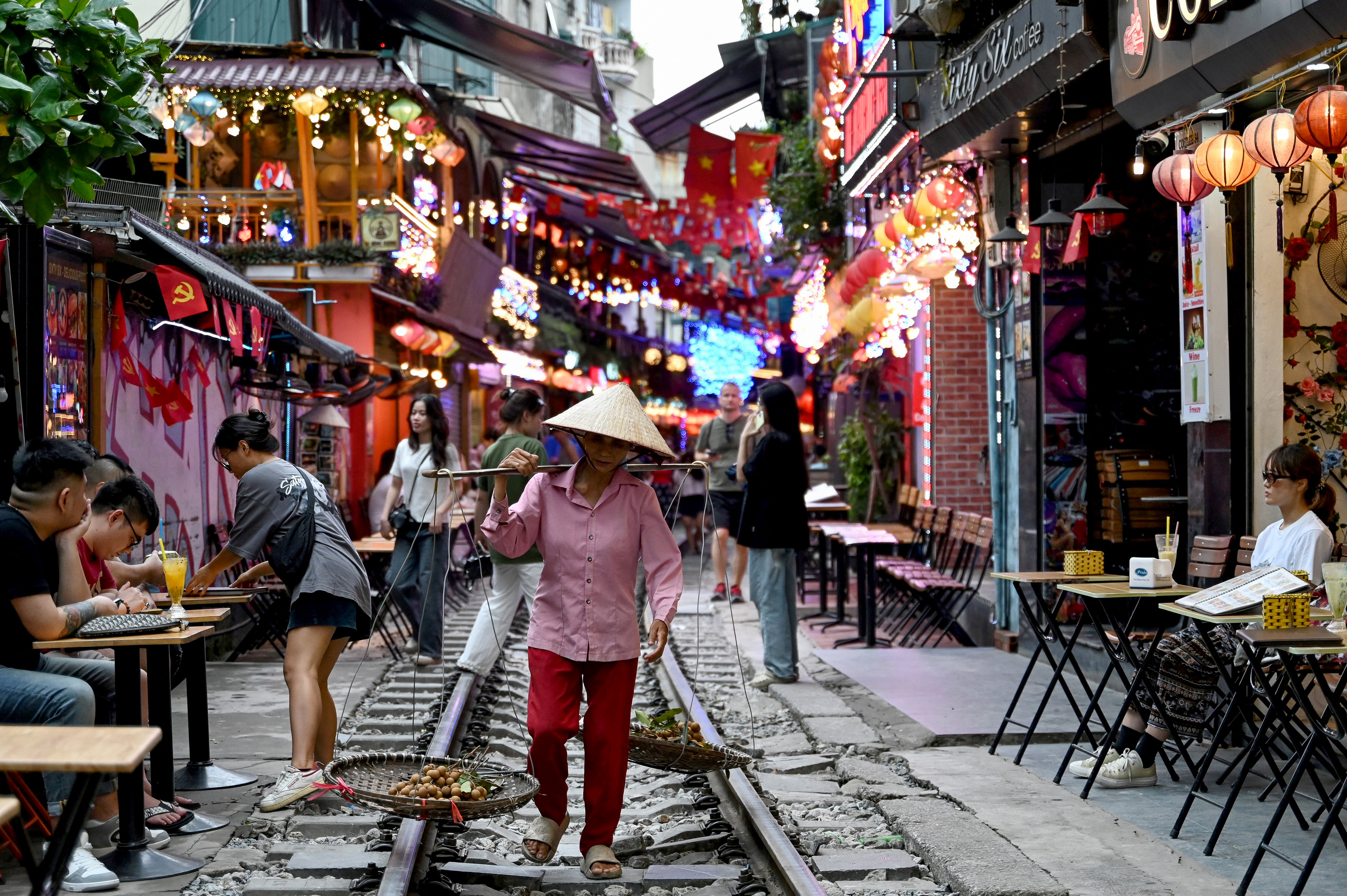 TOPSHOT - This photo taken on August 18, 2025 shows a street vendor walking along a railway track between cafe terraces in central Hanoi.