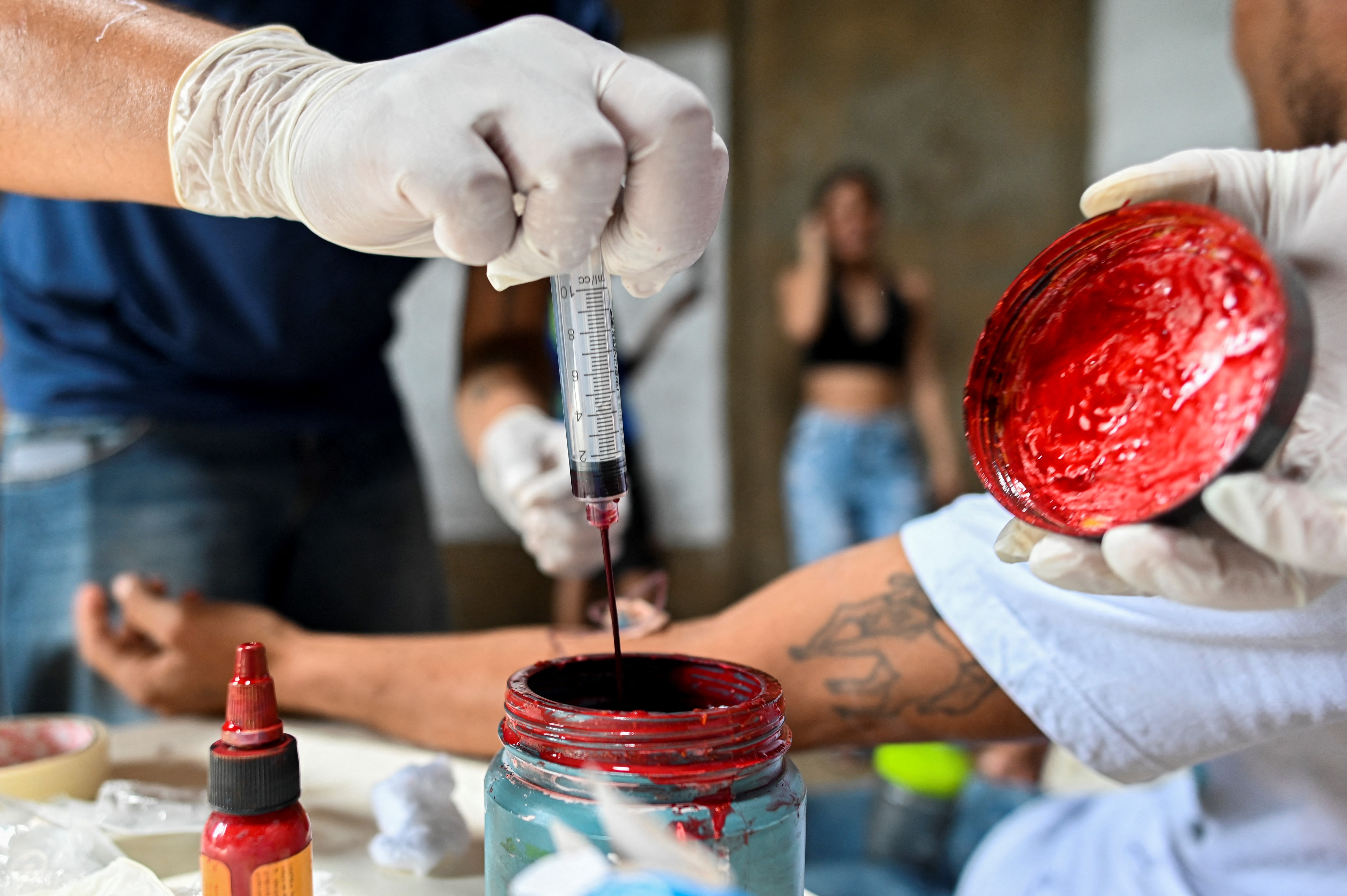 El artista colombiano Julián Castillo recolecta sangre humana, donada por voluntarios, para realizar murales. Los murales muestran al cantante puertorriqueño René Pérez,  Residente, y una paloma de la paz, en el barrio Siloé de Cali, el 23 de marzo de 2022, en rechazo a la violencia.
(Foto por Luis ROBAYO / AFP) /