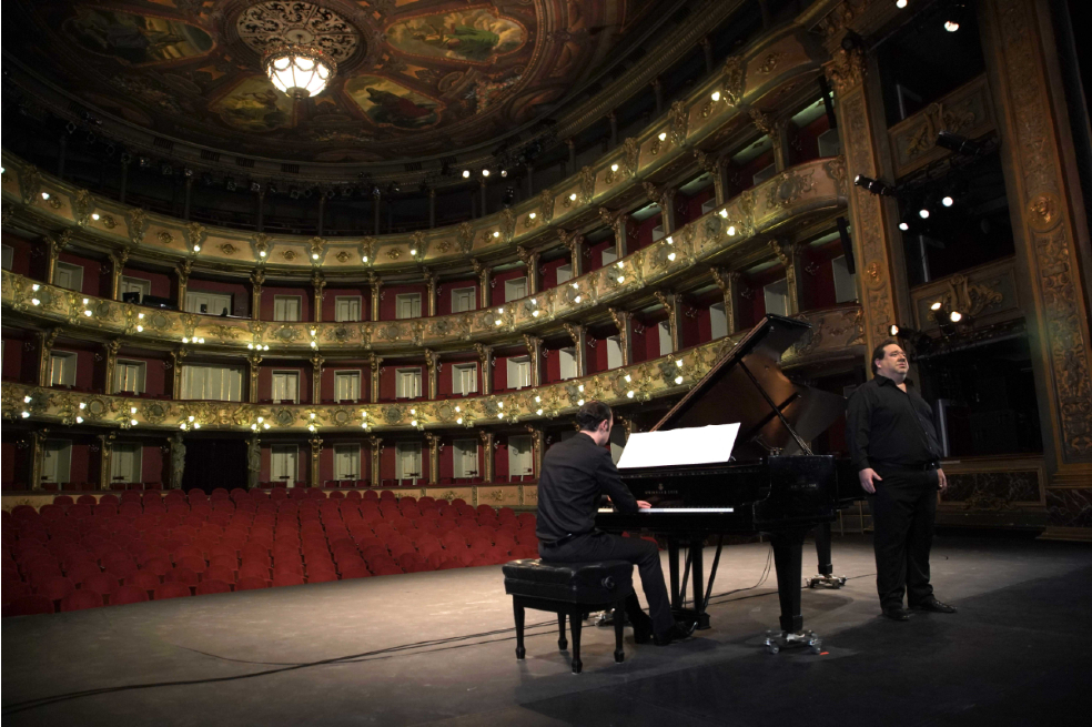 Valeriano Lanchas en el Teatro Colón. Él sale cantando al lado de un piano. De fondo, se ven las sillas rojas del teatro.