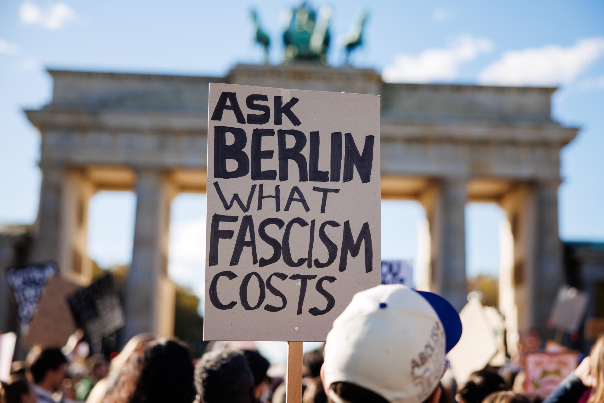Una persona sostiene un cartel que dice “Pregúntale a Berlín cuánto cuesta el fascismo” durante una manifestación frente a la Puerta de Brandeburgo en Berlín, Alemania.
