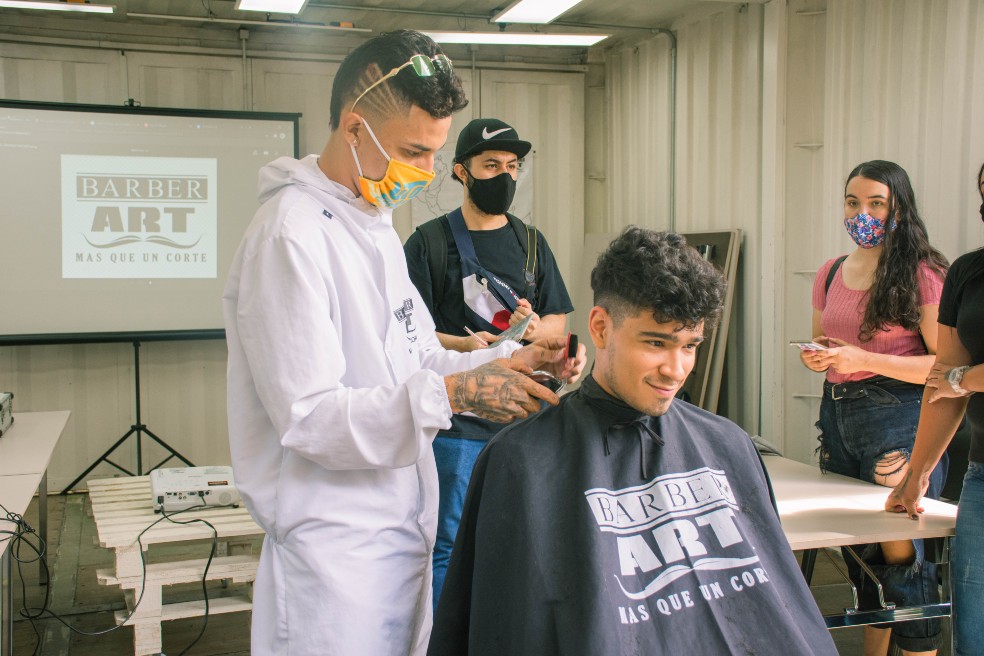 Un joven, protegido con una capa negra y sentado,  es atendido en Barber Art