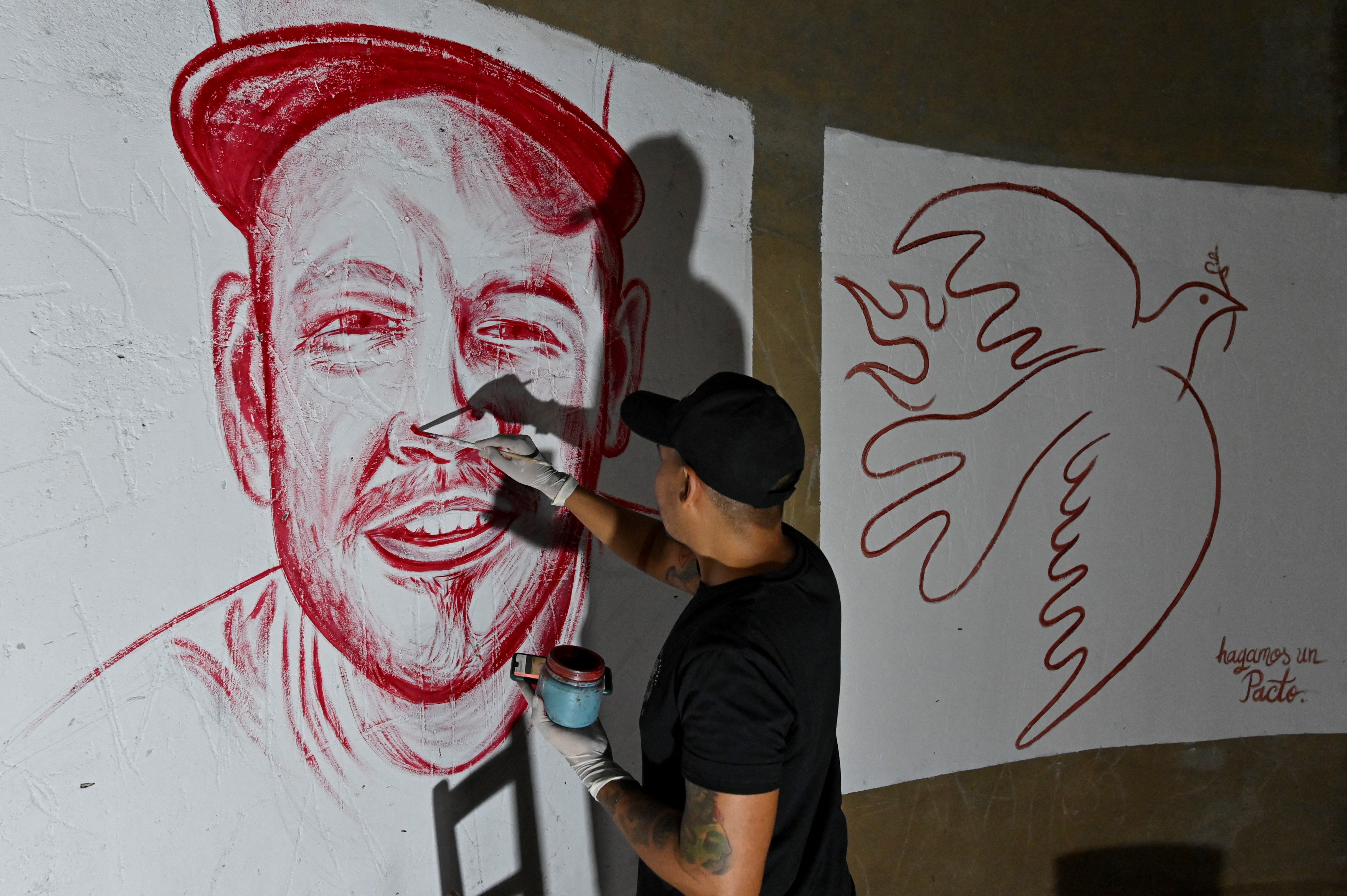 El artista colombiano Julián Castillo realiza sus murales pintados con sangre humana, que fue donada por voluntarios. Los murales muestran al cantante puertorriqueño René Pérez,  Residente, y una paloma de la paz, en el barrio Siloé de Cali, el 23 de marzo de 2022, en rechazo a la violencia.
(Foto por Luis ROBAYO / AFP) /