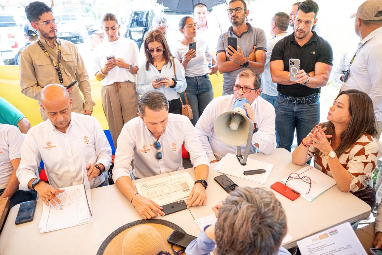 Delegación de la Agencia Nacional de Infraestructura reunida en Buenaventura. De derecha a izquierda: la ministra de Transporte, María Fernanda Rojas; Óscar Torres, presidente de la ANI; y Roberto Uparela, vicepresidente ejecutivo de la ANI. Los funcionarios, vestidos con camisas blancas institucionales, participan en un encuentro público alrededor de una mesa, mientras asistentes registran la escena con teléfonos móviles.