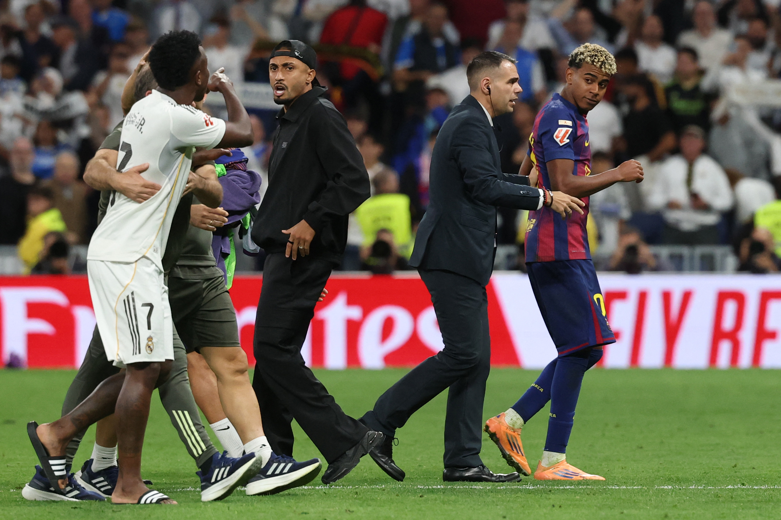 El delantero brasileño #07 del Real Madrid Vinicius Junior (izq.) discute con el delantero brasileño #11 del Barcelona Raphinha (centro) y el delantero español #10 del Barcelona Lamine Yamal (der.) al final del partido de fútbol de la liga española entre el Real Madrid CF y el FC Barcelona en el estadio Santiago Bernabéu en Madrid el 26 de octubre de 2025.