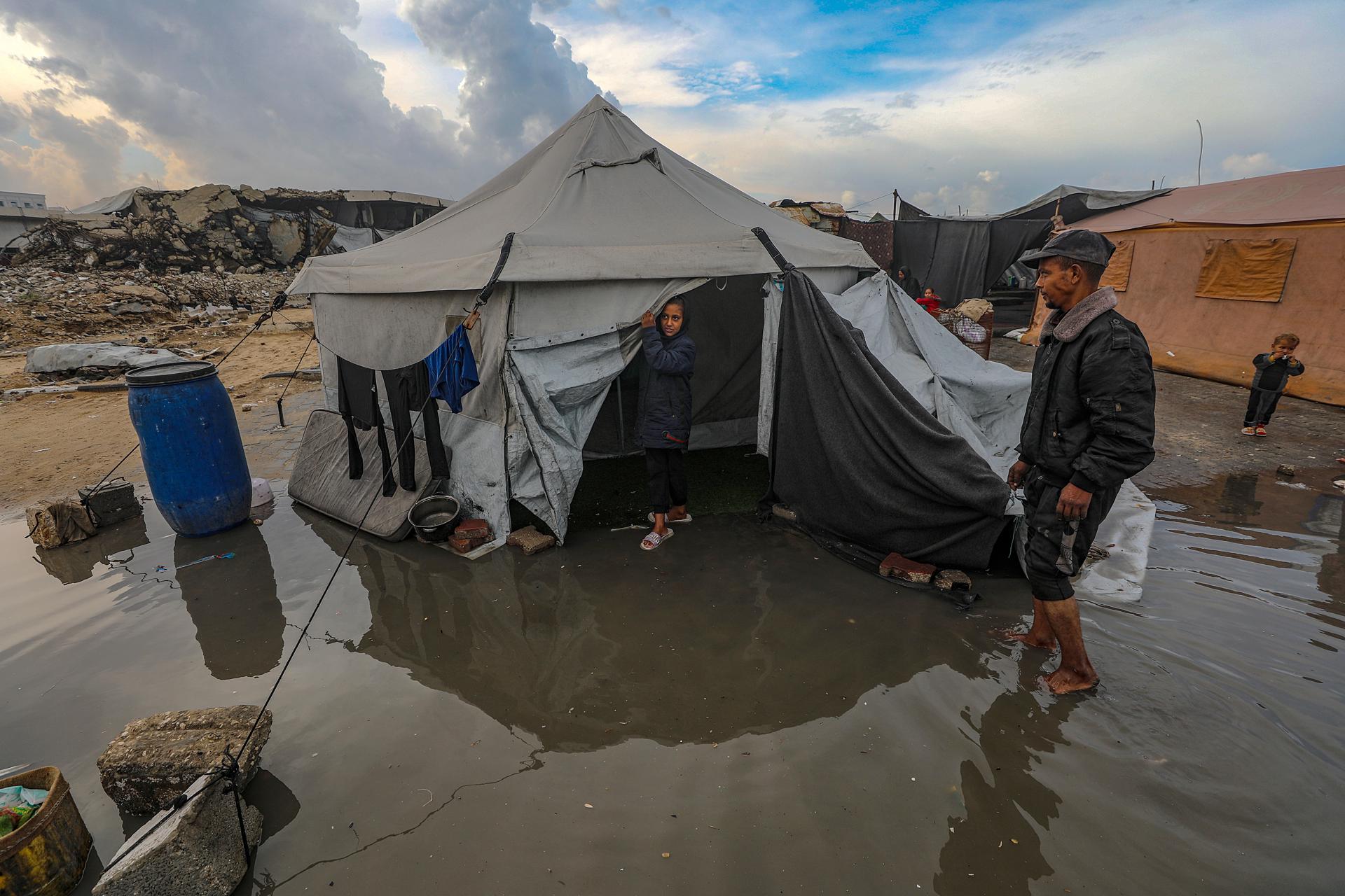 GAZA CITY (---), 14/11/2025.- Internally displaced Palestinians from northern and eastern Gaza walk through a puddle outside their tent during a rainy day at a makeshift camp west of Gaza City, Gaza Strip, 14 November 2025. Around 1.9 million people in Gaza, nearly 90 percent of the population, have been displaced since the Israel-Hamas conflict began in October 2023, according to the UN. EFE/EPA/MOHAMMED SABER
