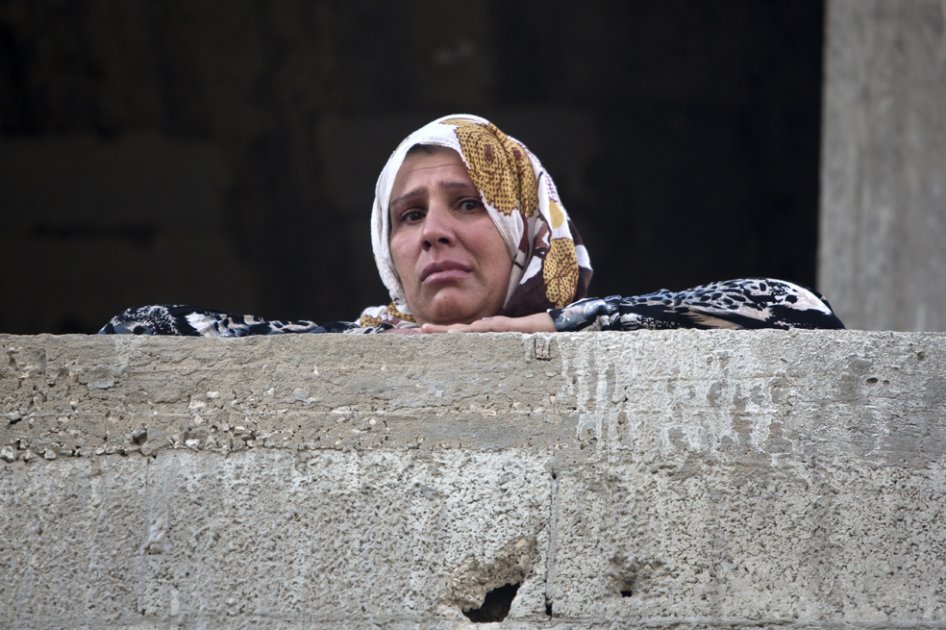 Una mujer palestina mira desde el balcón un carro destruido por el ataque israelí a la ciudad de Gaza. 