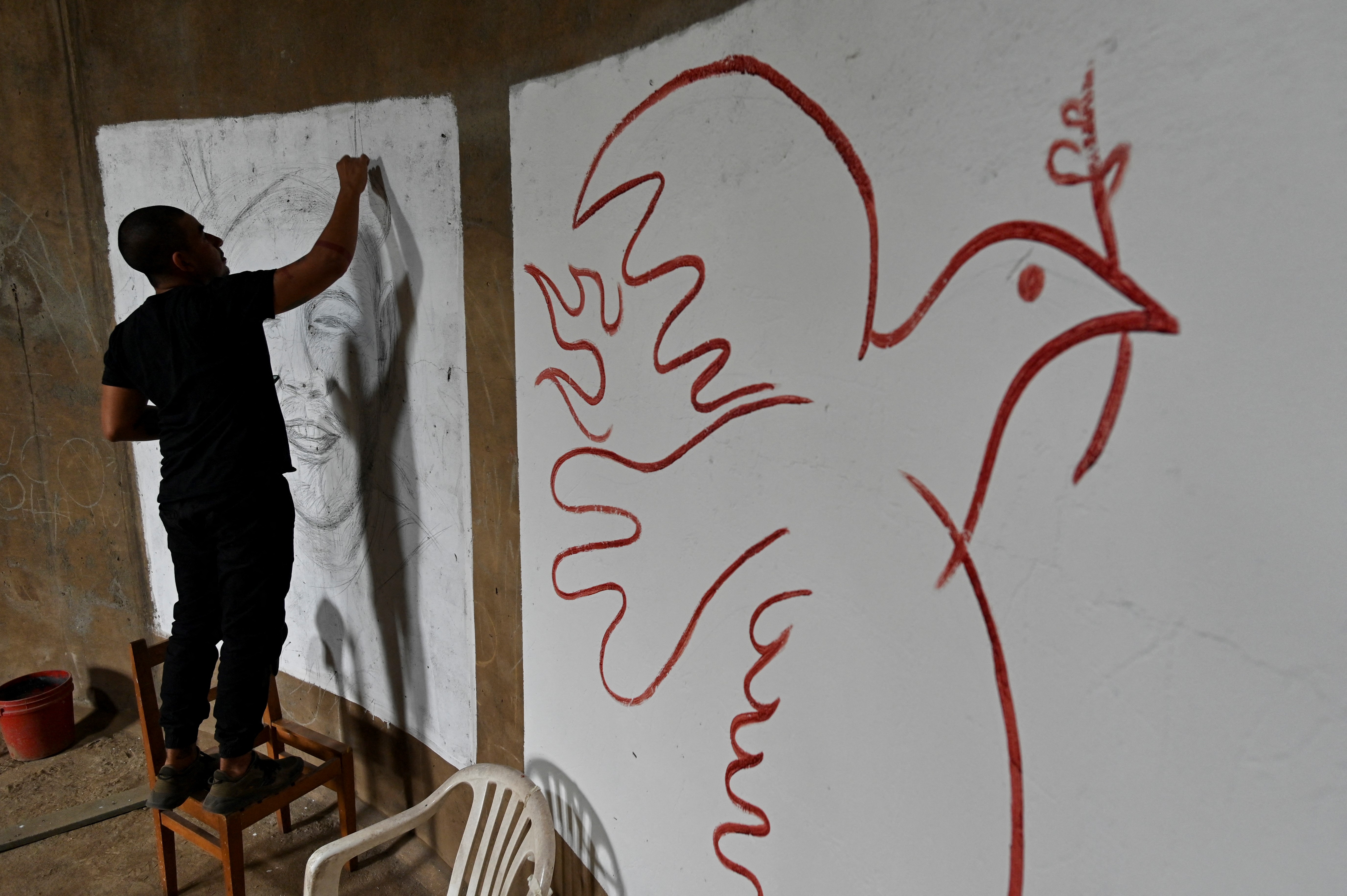 El artista colombiano Julián Castillo dibuja un mural del cantante puertorriqueño  René Pérez, Residente, antes de pintarlo con sangre humana donada por voluntarios. Una paloma de la paz se pintó al lado, en el barrio Siloé en Cali, el 23 de marzo de 2022, en rechazo a la violencia. 
(Foto por Luis ROBAYO / AFP)