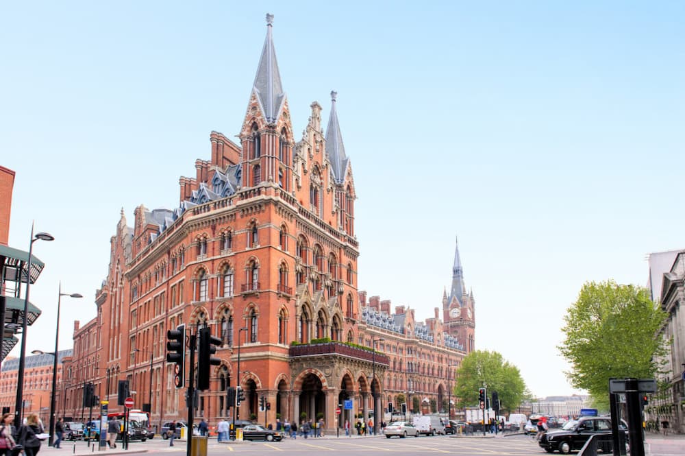La St Pancras International es una de las estaciones más emblemáticas de Londres, reconocible por su imponente fachada neogótica de ladrillo rojo diseñada en el siglo XIX por George Gilbert Scott. Inaugurada en 1868 para conectar la capital con las Midlands, destaca por su espectacular bóveda de hierro —la más grande del mundo en su época— y por su transformación en terminal del Eurostar, que hoy enlaza Londres con ciudades como París o Bruselas. Más allá de su función ferroviaria, su estética, su historia y su presencia en el cine la han convertido en un verdadero icono urbano.