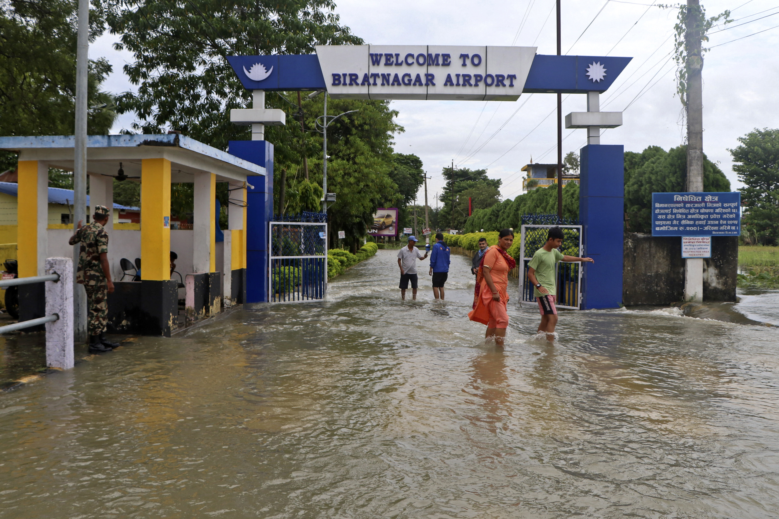 People wade through the flooded entrance gate of a domestic airport after heavy rains in Biratnagar on October 20, 2021, as the death toll from days of flooding and landslides in India and Nepal crossed 100. (Photo by Lila Ballav Ghimire / AFP)