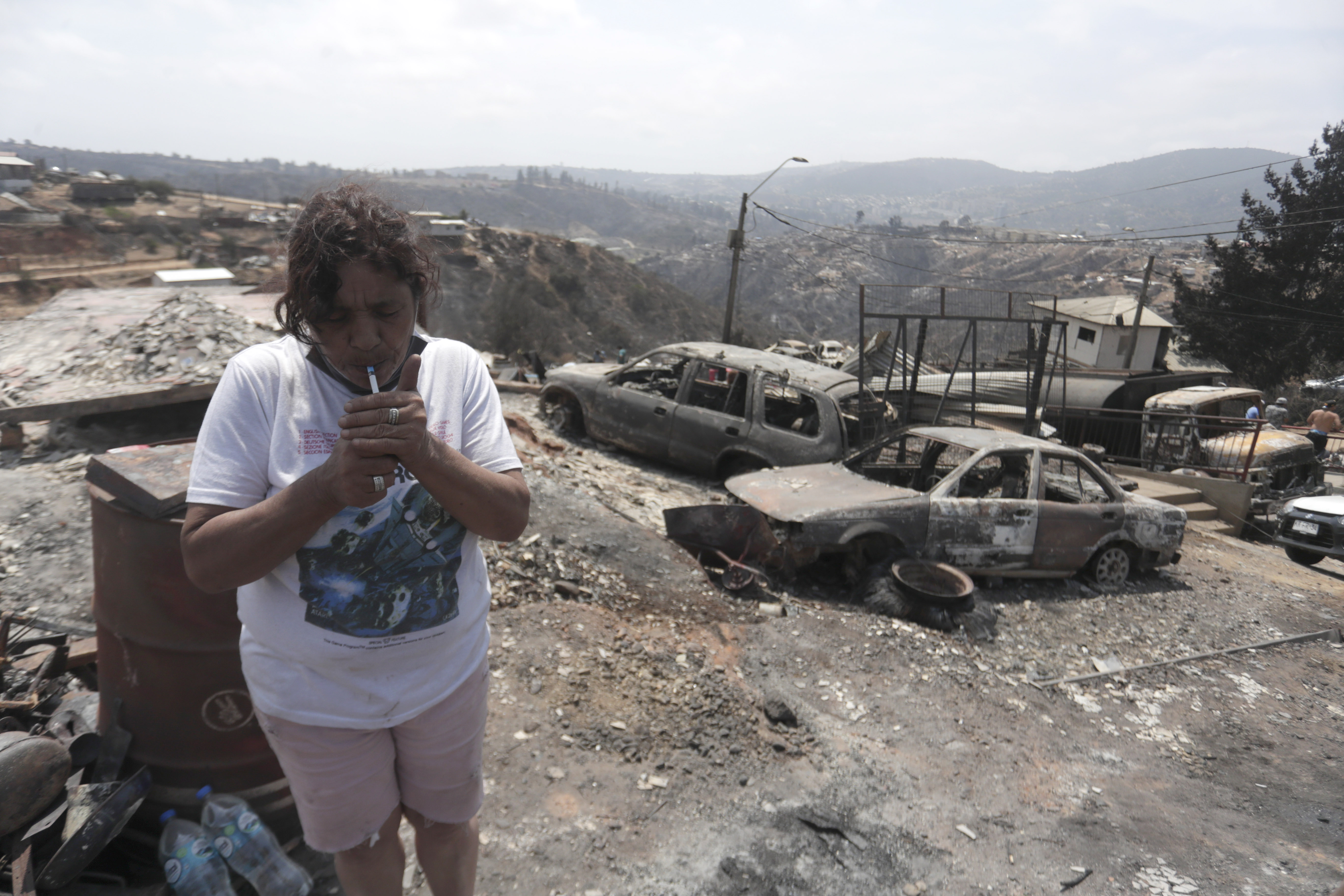 AME5705. VIÑA DEL MAR (CHILE), 04/02/2024.- Una mujer enciende un cigarrillo en el campamento irregular “Pompeya” cerca de los escombros, tras los incendios del día viernes 2 de febrero, en la zona de Viña del Mar, Región de Valparaiso (Chile). En el campamento irregular “Pompeya”, uno de las “zona cero” de los mortíferos que han arrasado miles de casas y segado la vida de más de medio centenar de personas en la región costera de Valparaiso, apenas se escuchan ya lamentos. EFE/ Ailen Díaz