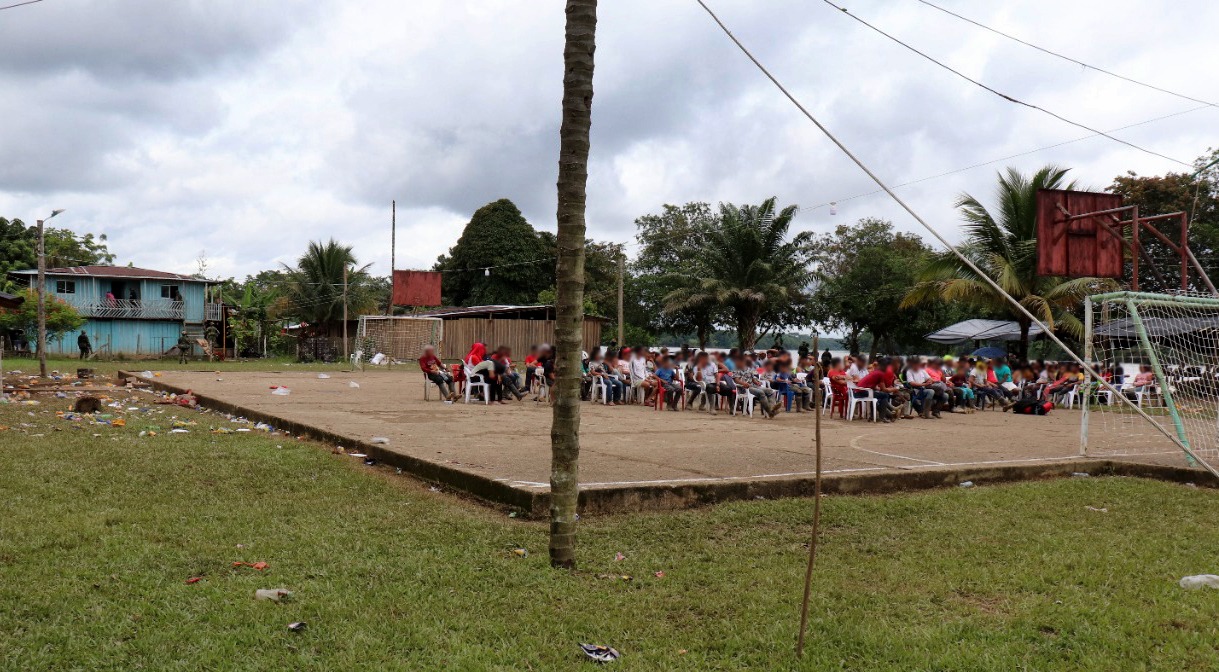 Esta fotografía, que está en poder de las autoridades, demostaría que la población civil de la vereda Alto Remanso sí estuvo retenida en el polideportivo. Como narran en sus testimonios, los habrían obligado a sentarse dando la espalda a la vereda y mirando hacia el río y la selva. En esta imagen se ve la presencia de menores de edad. Al fondo de la imagen, casi sobre la orilla del río, se puede observar la presencia de dos militares.