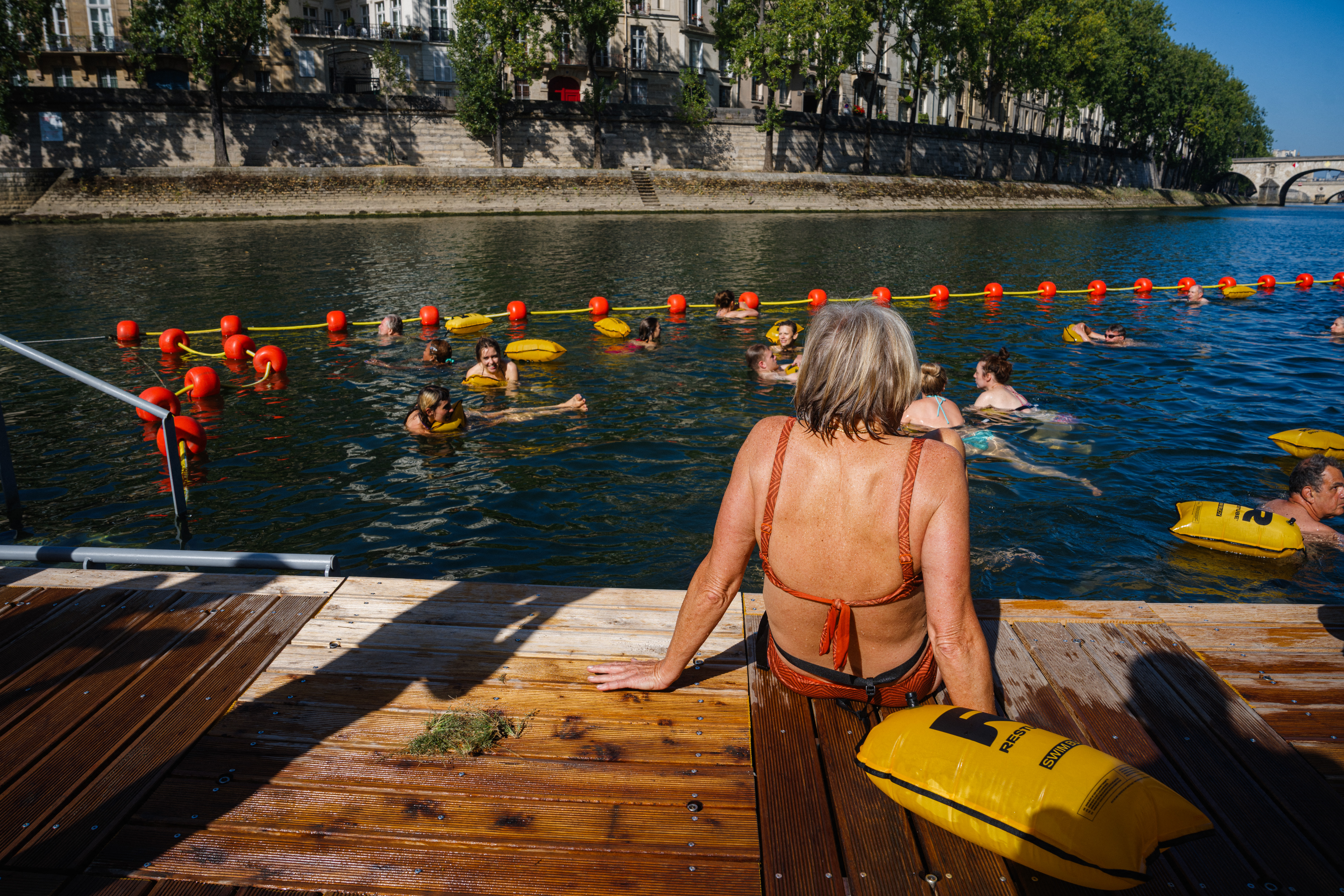 People swim as a woman sunbathes on the docks at the Bras Marie safe bathing site on the river Seine in Paris on August 12, 2025.