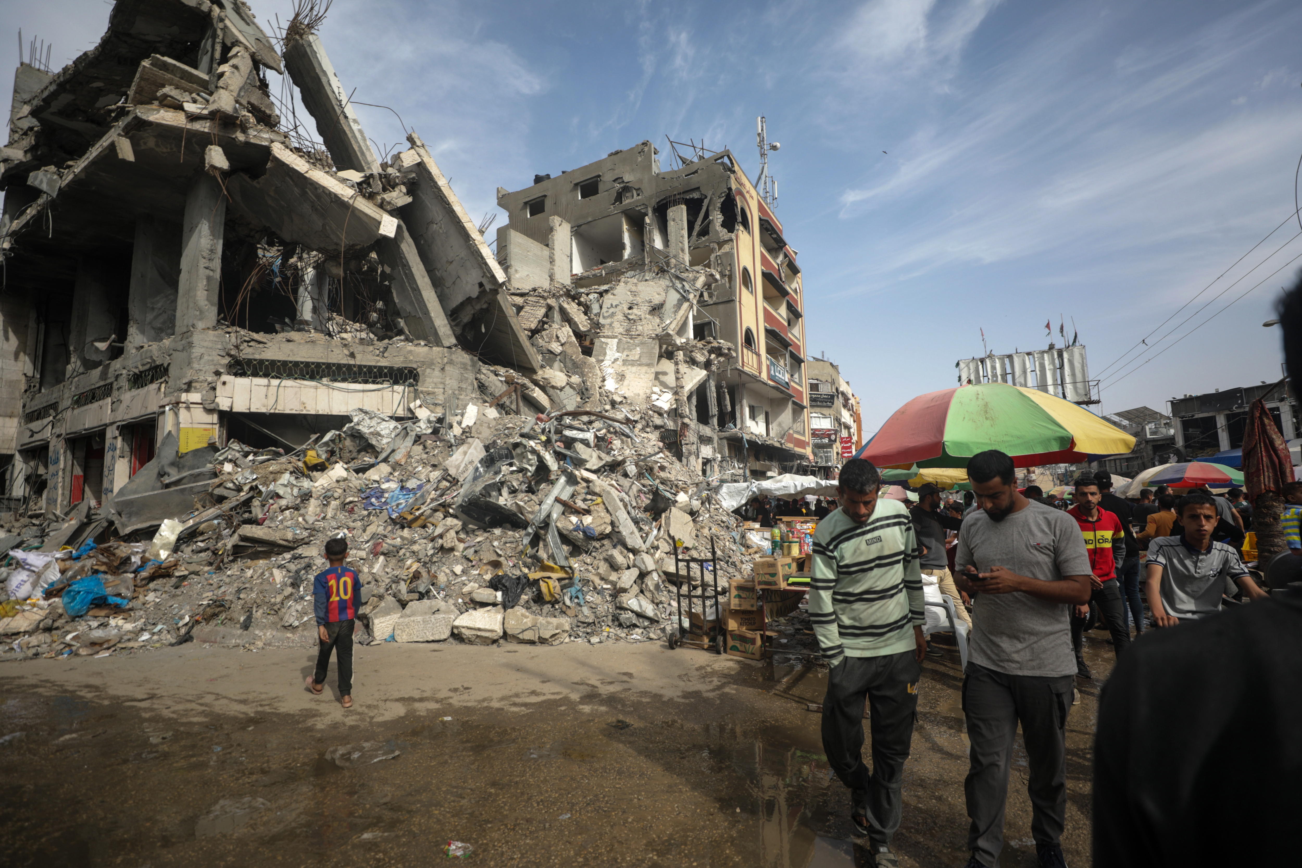 Al Nusairat (---), 05/04/2024.- Palestinians walk past kiosks set up next to destroyed buildings on the last Friday of Ramadan along a street in Al Nusairat refugee camp, Gaza Strip, 05 April 2024. More than 33,000 Palestinians and over 1,450 Israelis have been killed, according to the Palestinian Health Ministry and the Israel Defense Forces (IDF), since Hamas militants launched an attack against Israel from the Gaza Strip on 07 October 2023, and the Israeli operations in Gaza and the West Bank which followed it. Up to 1.9 million people have been displaced throughout the Gaza Strip. EFE/EPA/MOHAMMED SABER