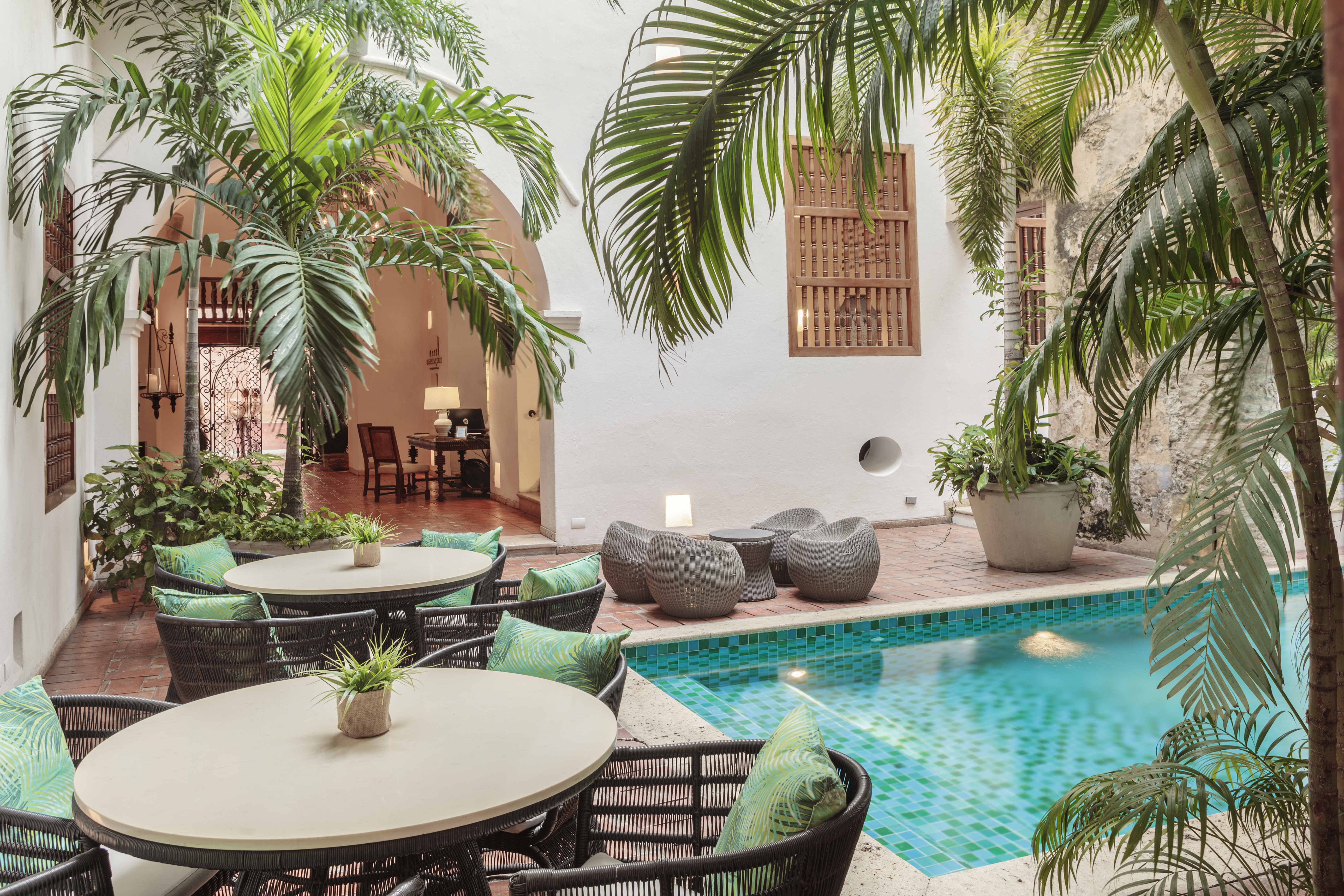 Imagen de un hotel con piscina, palmeras y mesas alrededor.