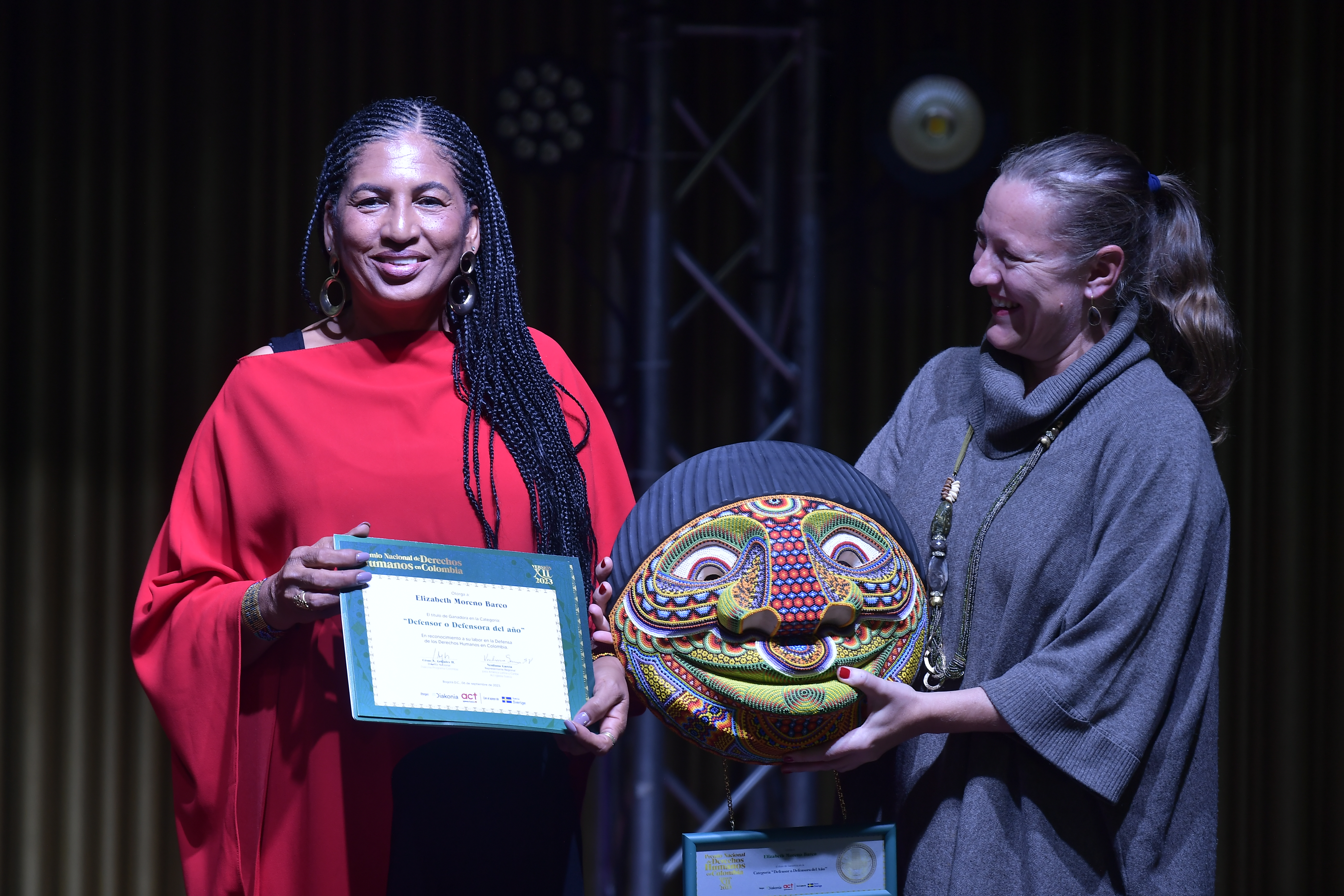 Lidera el Consejo Comunitario General del San Juan (Acadesan) (vestido rojo), recibe de Helena Storm, embajadora de Suecia en Colombia (vestido gris), el premio a la defensora del año, del Premio Nacional de Derechos Humanos XII 2023 en Colombia.