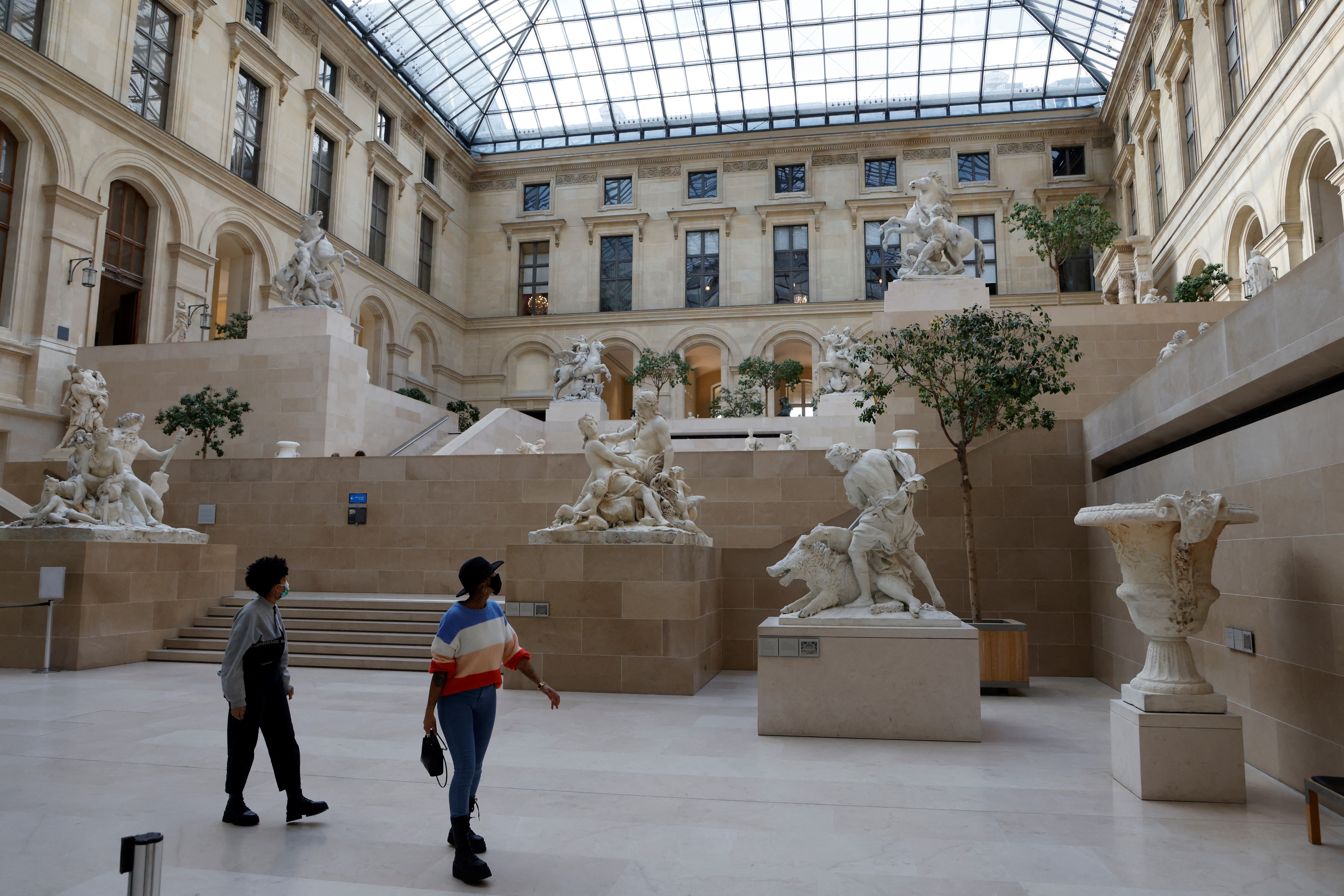 (FILES) Visitors wearing protective face masks look at statues inside the deserted Louvre Museum as the novel coronavirus Covid-19 pandemic keeps the tourists away, in Paris on October 14, 2020.