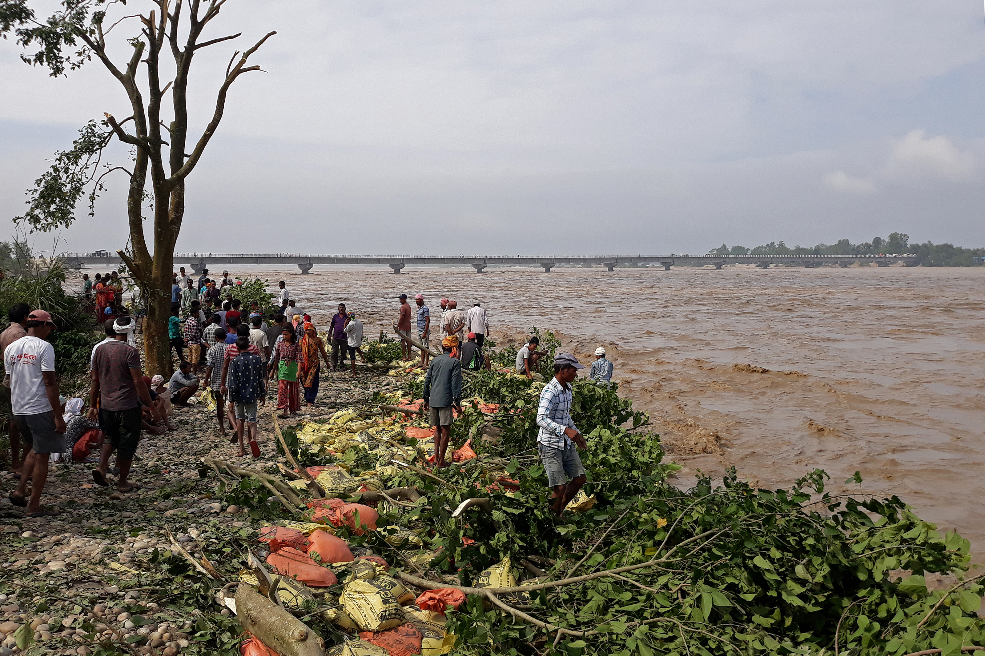 People stand along the banks of flooded Karnali river following heavy rains in Rajapur village of Bardiya district in Nepal on October 20, 2021, as the death toll from days of flooding and landslides in India and Nepal crossed 100. (Photo by KRISHNA ADHIKARI / AFP)