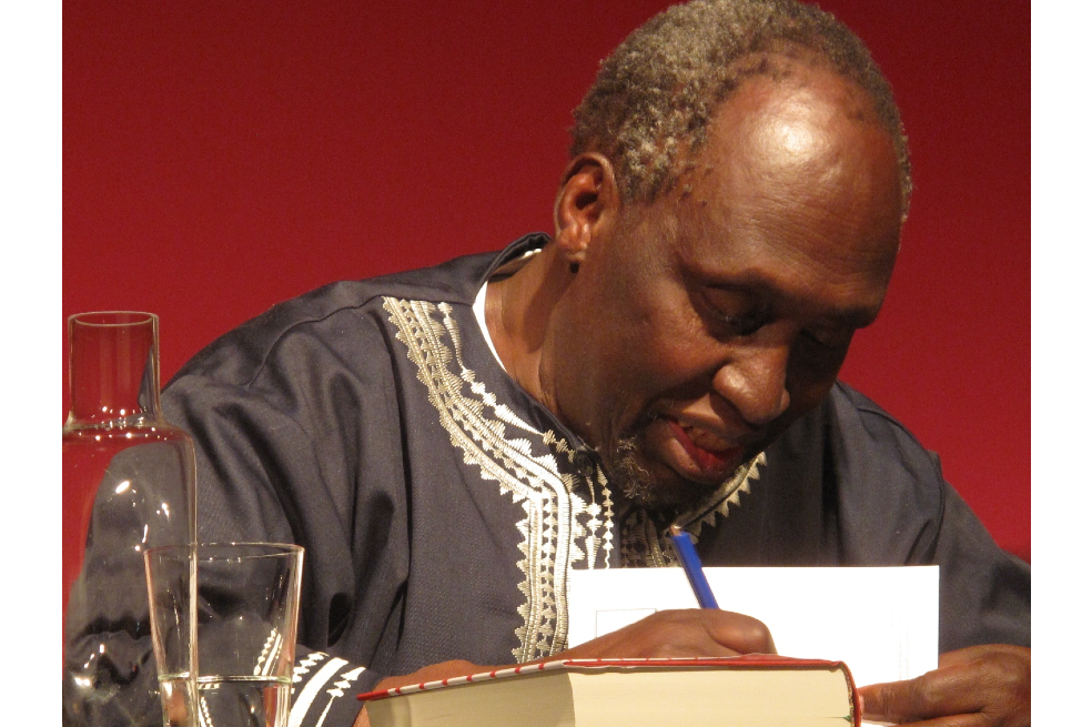 Ngũgĩ wa Thiong'o tiene su mirada hacia abajo y parece estar firmando un libro.