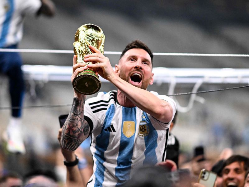 Argentina's forward #10 Lionel Messi lifts the FIFA World Cup Trophy as he celebrates with supporters winning the Qatar 2022 World Cup final football match between Argentina and France at Lusail Stadium in Lusail, north of Doha on December 18, 2022. (Photo by Kirill KUDRYAVTSEV / AFP)
