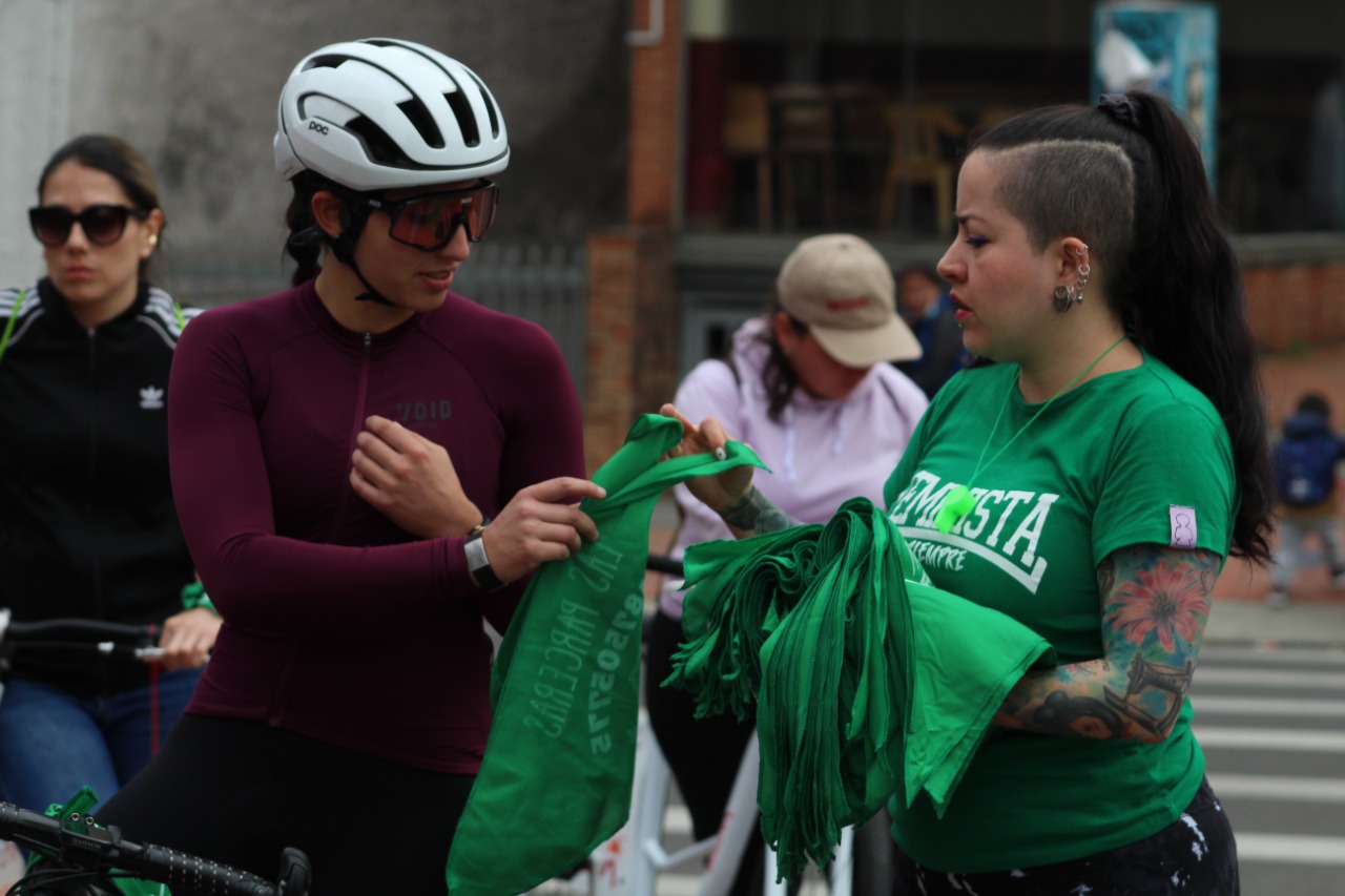 Una mujer entrega a otra una pañoleta verde