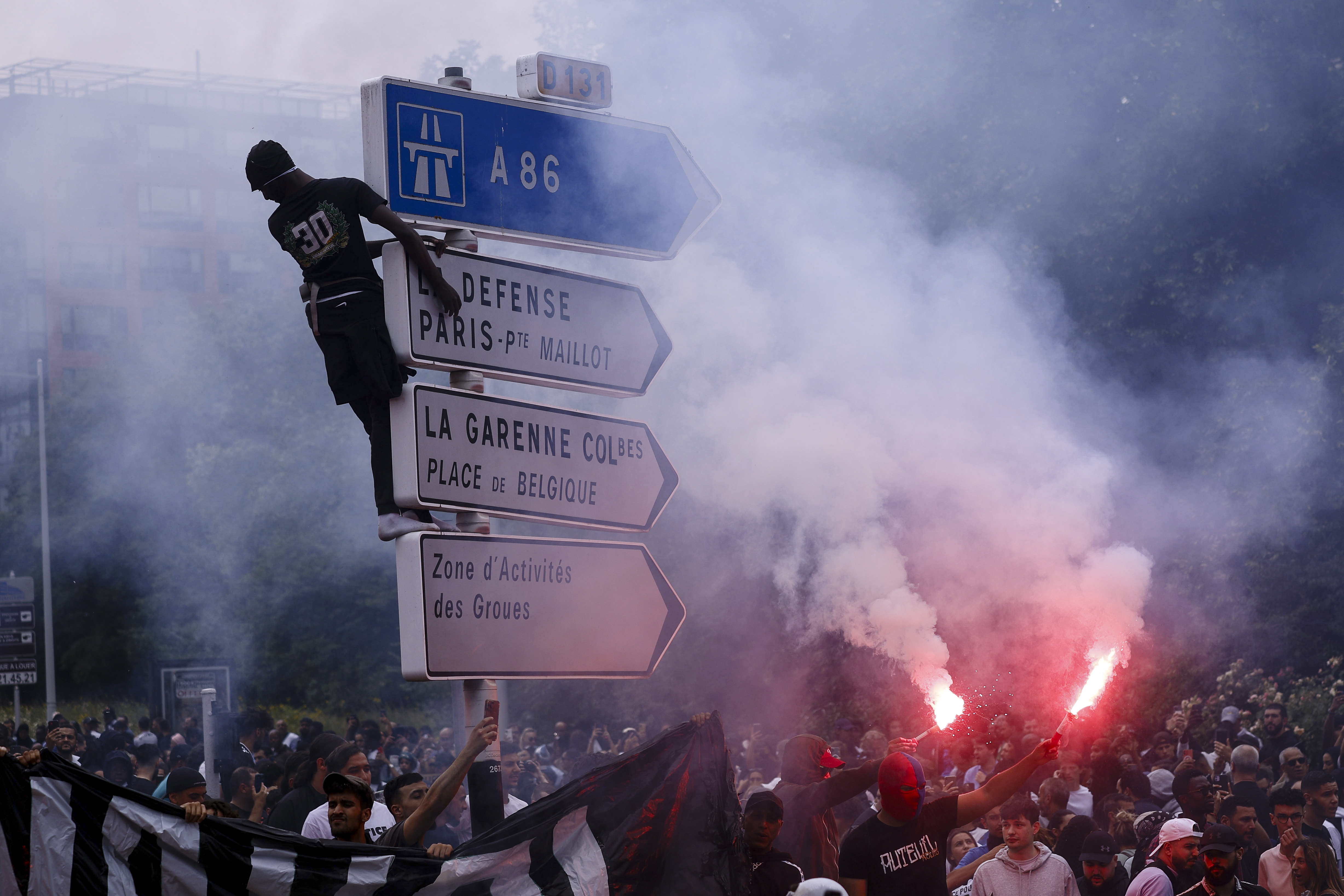 Nanterre (France), 29/06/2023.- A person climbs a traffic sign as others hold flares during a march in the memory of 17-year-old Nahel, who was killed by French Police in Nanterre, near Paris, France, 29 June 2023. Violence broke out after the police fatally shot a 17-year-old during a traffic stop in Nanterre on 27 June. According to the French interior minister, 31 people were arrested with 2,000 officers being deployed to prevent further violence. (Disturbios, Francia) EFE/EPA/YOAN VALAT
