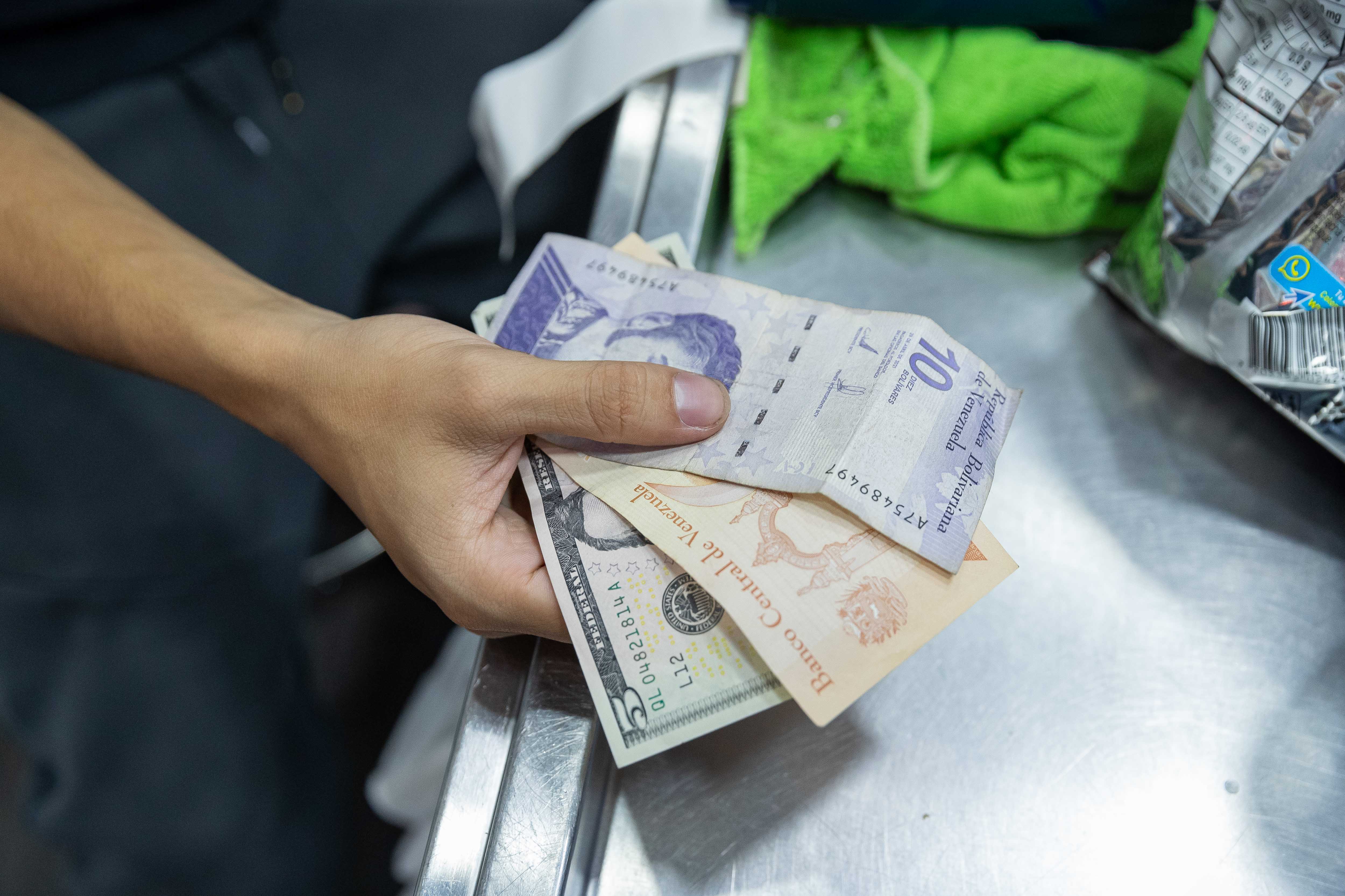 AME463. CARACAS (VENEZUELA), 09/07/2024.- Un hombre paga en una tienda con billetes de dolares estadounidenses y bolívares soberanos, el 8 de julio de 2024, en Caracas (Venezuela). La inflación en Venezuela, que en junio cayó hasta el 1 %, se ha desacelerado a raíz de una política para estabilizar el precio del dólar -divisa usada en el país para cotizar bienes y servicios-, para lo que también se han "sacrificado" salarios y créditos bancarios, advierten expertos. EFE/ Ronald Peña