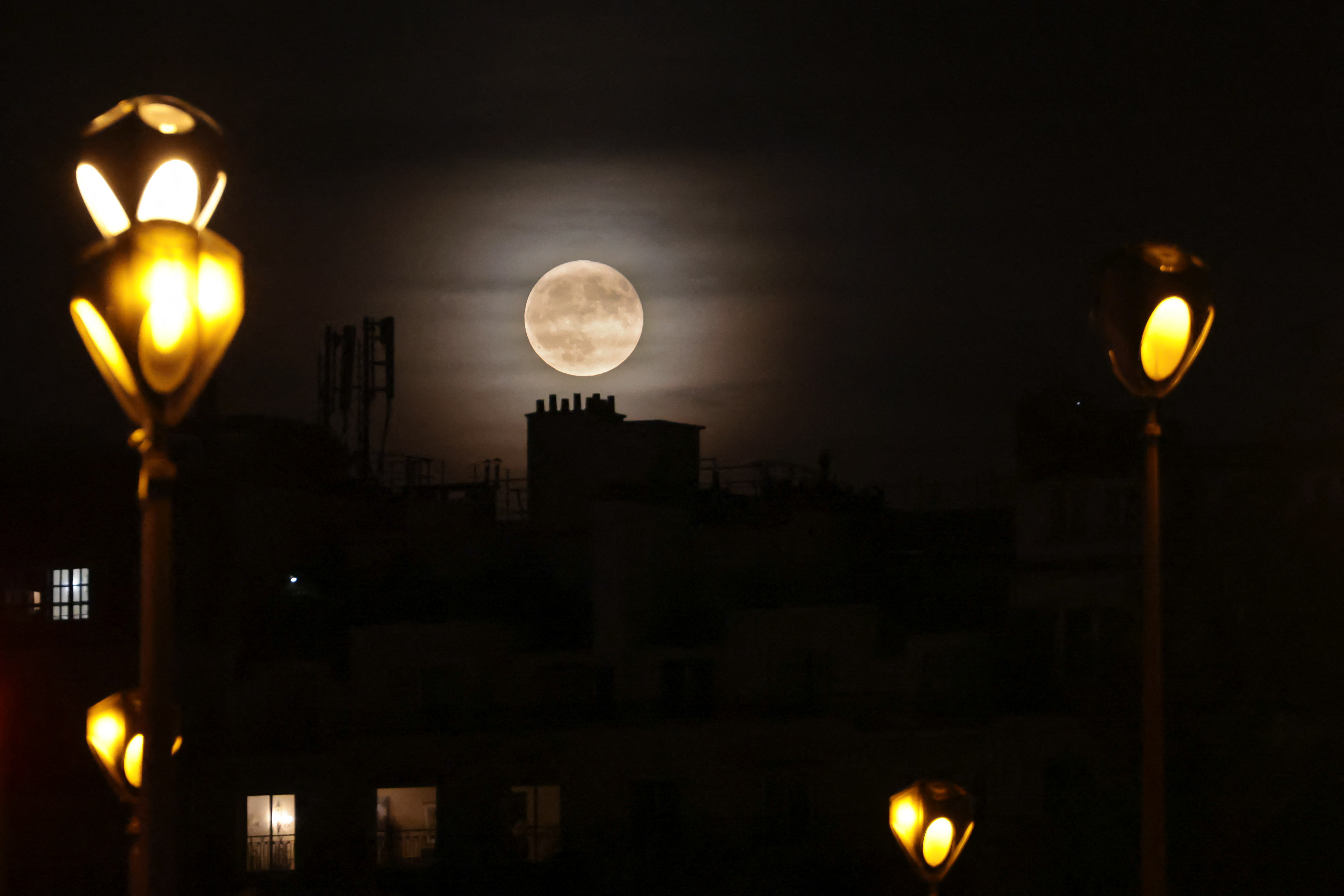 La luna llena conocida como «luna de fresa» se eleva sobre tejados y farolas en París el 11 de junio de 2025.