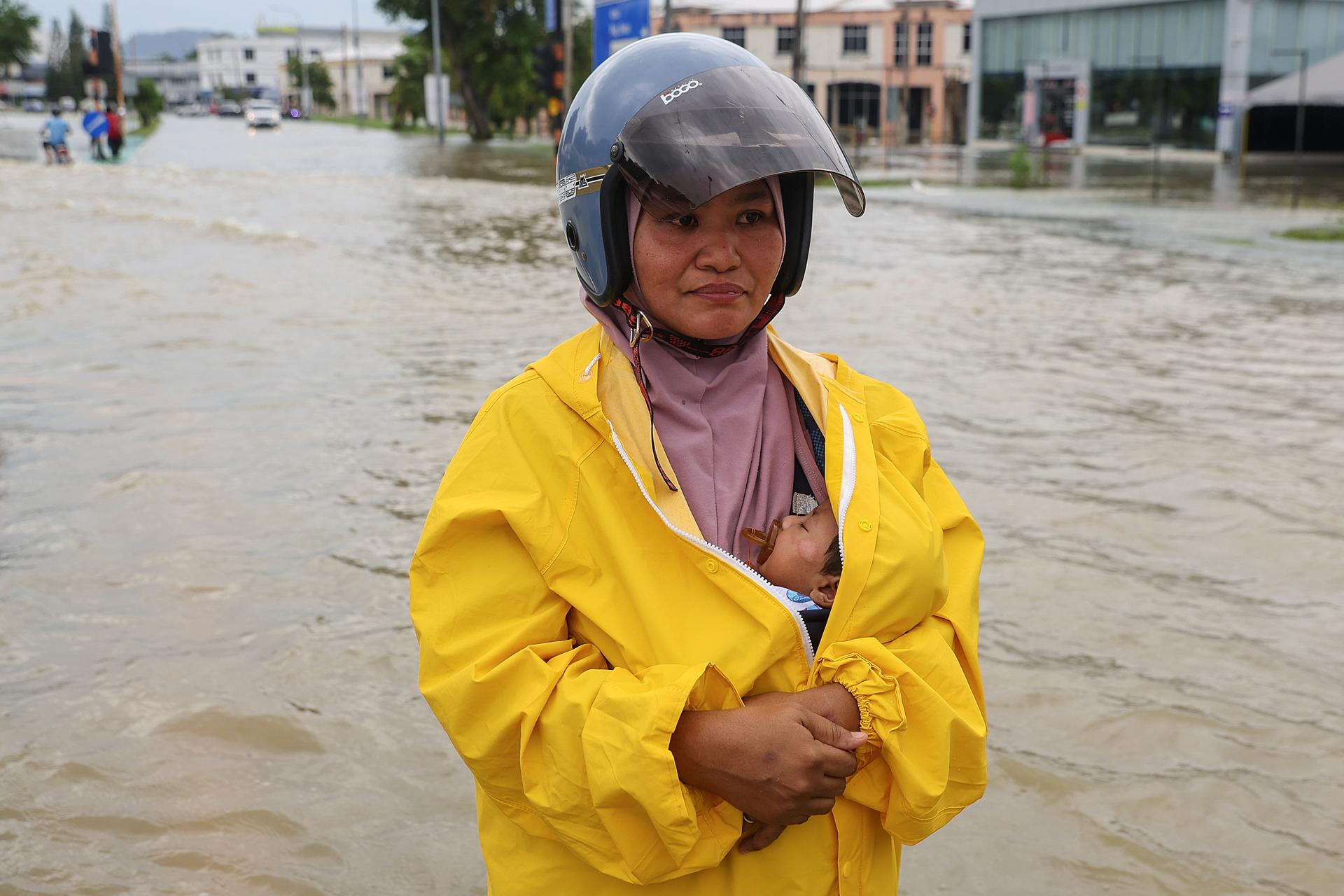 KANGAR (Malaysia), 27/11/2025.- A woman carries a child as she wades through floodwaters at the town of Kangar, state of Perlis, Malaysia, 27 November 2025. According to data from the government disaster information website on 27 November, more than 28,000 people have been evacuated across seven states. (Inundaciones, Malasia) EFE/EPA/FAZRY ISMAIL