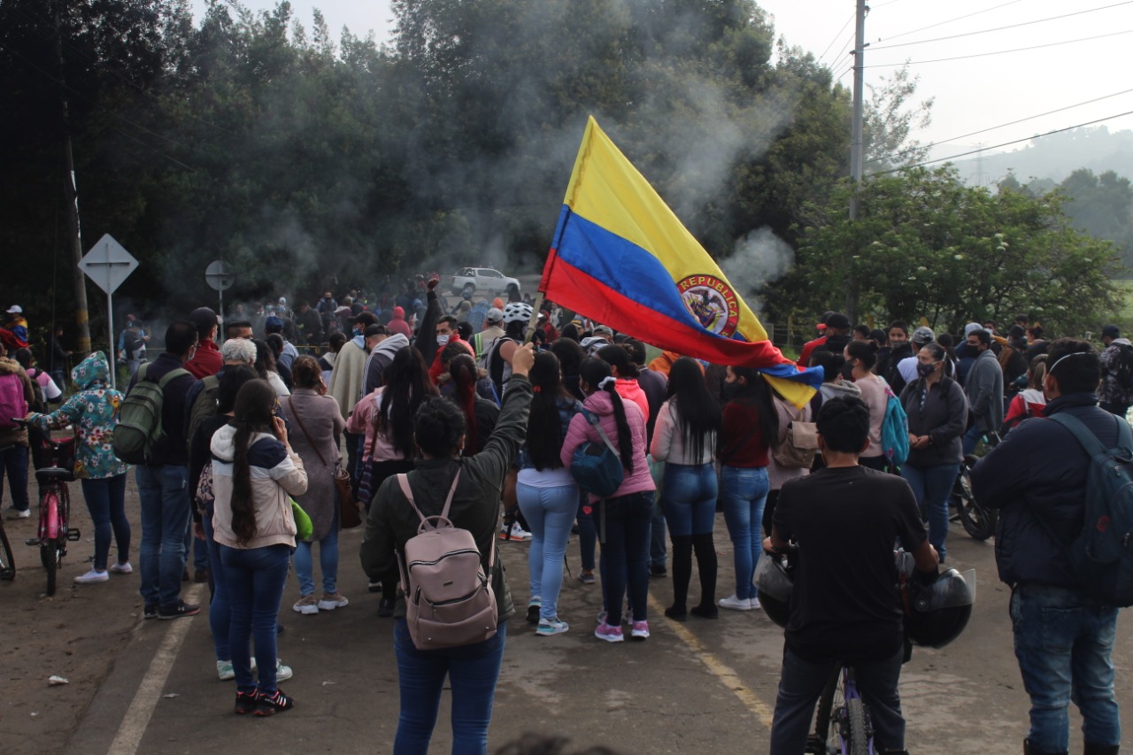 Varias personas de espalda sobre la vía. Una de ella alza una bandera de Colombia