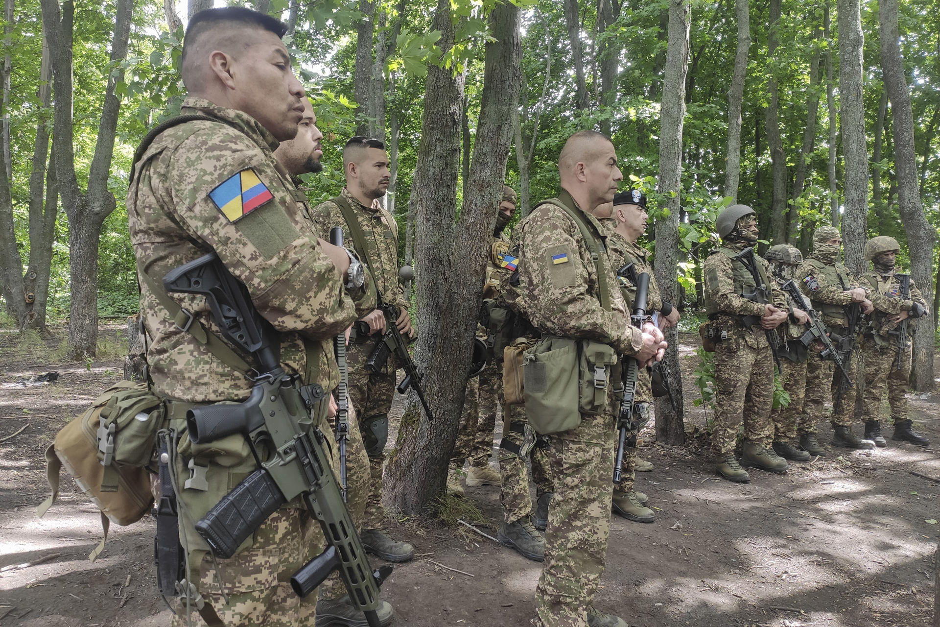 JÁRKOV, 18/07/2025.- En un campo de entrenamiento boscoso en la región ucraniana de Járkov, en el este del país, un grupo de hombres uniformados, muchos con parches que los identifican como colombianos, escucha atentamente a su instructor ucraniano. Son parte de la unidad 'Guajiro', un contingente de combatientes extranjeros dentro de la Brigada Jartia de la Guardia Nacional de Ucrania. EFE/ Rostyslav Averchuk