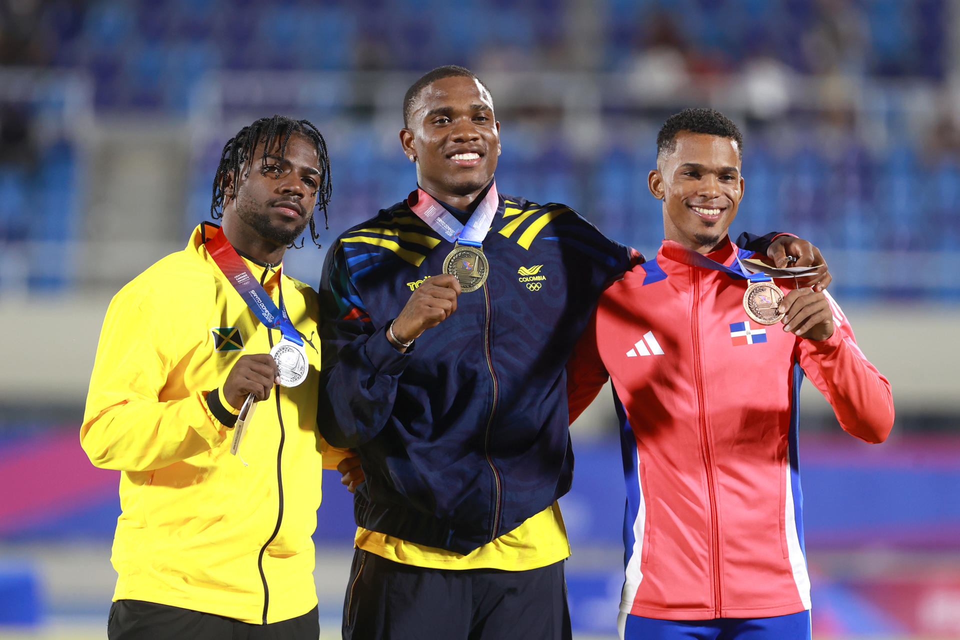AME5680. SANTO DOMINGO (REPÚBLICA DOMINICANA), 03/08/2026.- Ronal Longa (c) de Colombia, medalla de oro, Bouwahjgie Mkrumie (i) de Jamaica, medalla de plata, y Melbin Marcelino de República Dominicana, medalla de bronce, posan en la ceremonia de premiación de los 100 m Masculino este lunes, durante los XXV Juegos Centroamericanos y del Caribe Santo Domingo 2026, en Santo Domingo (República Dominicana). EFE/ Orlando Barría
