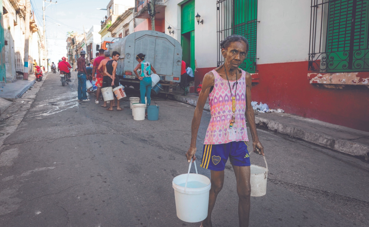 Un residente transporta cubos de agua pasando junto a personas que hacen fila al lado de un camión cisterna en un barrio de Matanzas, Cuba, el 6 de agosto de 2026. Foto: AFP