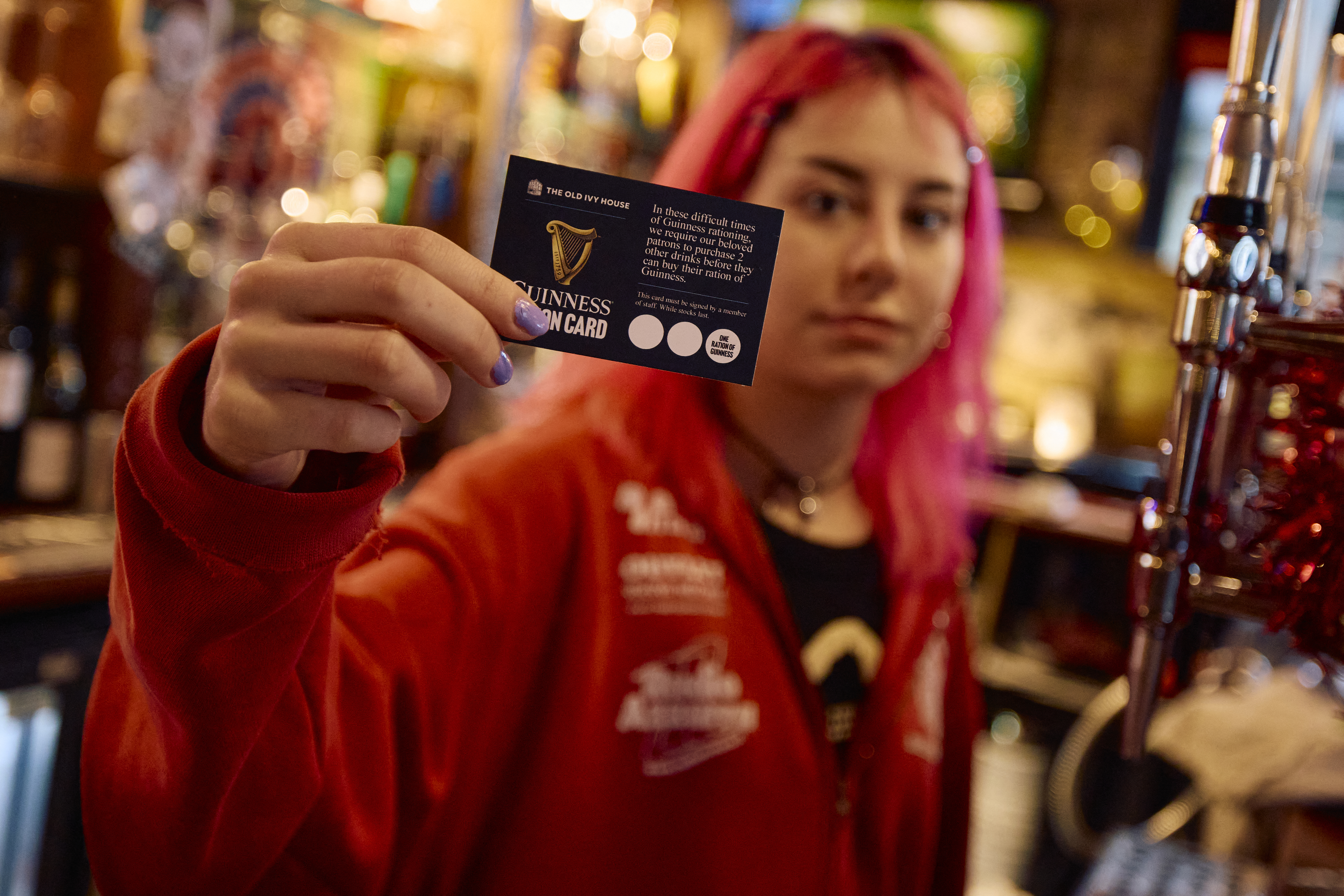 Kate Davidson, detrás de la barra de su pub en Londres, sostiene tarjetas de racionamiento de Guinness, implementadas ante la escasez de esta cerveza en Reino Unido.