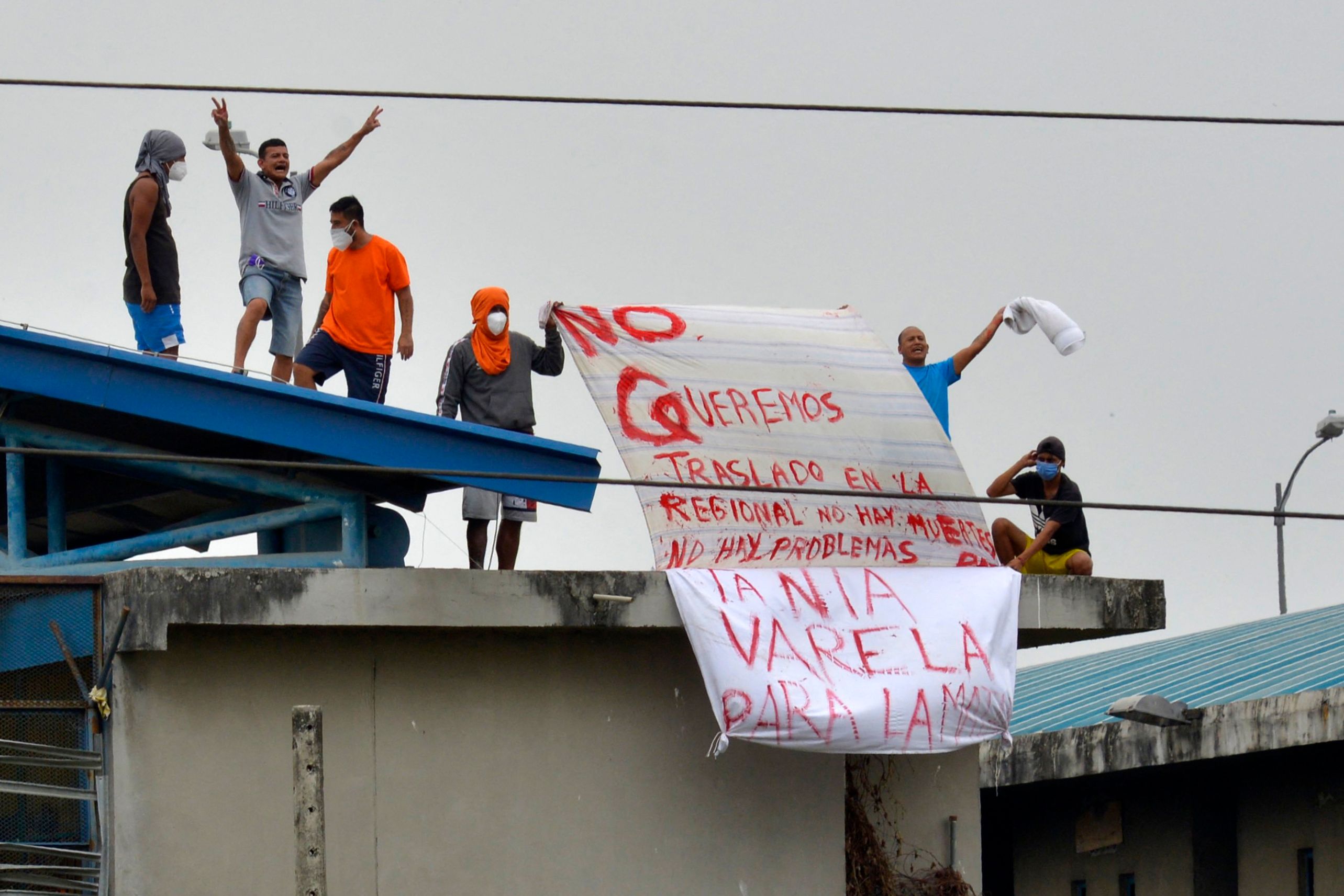 TOPSHOT - Inmates hold signs while standing atop a roof at the Regional 8 prison, next to the penitentiary, in the outskirts of Guayaquil, Ecuador, on October 2, 2021. - Inmates fired at police officers this Saturday in the same prison that a riot left at least 118 dead, including six beheaded, earlier this week. Ecuador deployed on the eve thousands of police and soldiers to secure its violent prisons as relatives of convicts caught up in one of South America's deadliest inmate riots clamored for news about their fate. (Photo by Fernando M�ndez / AFP)