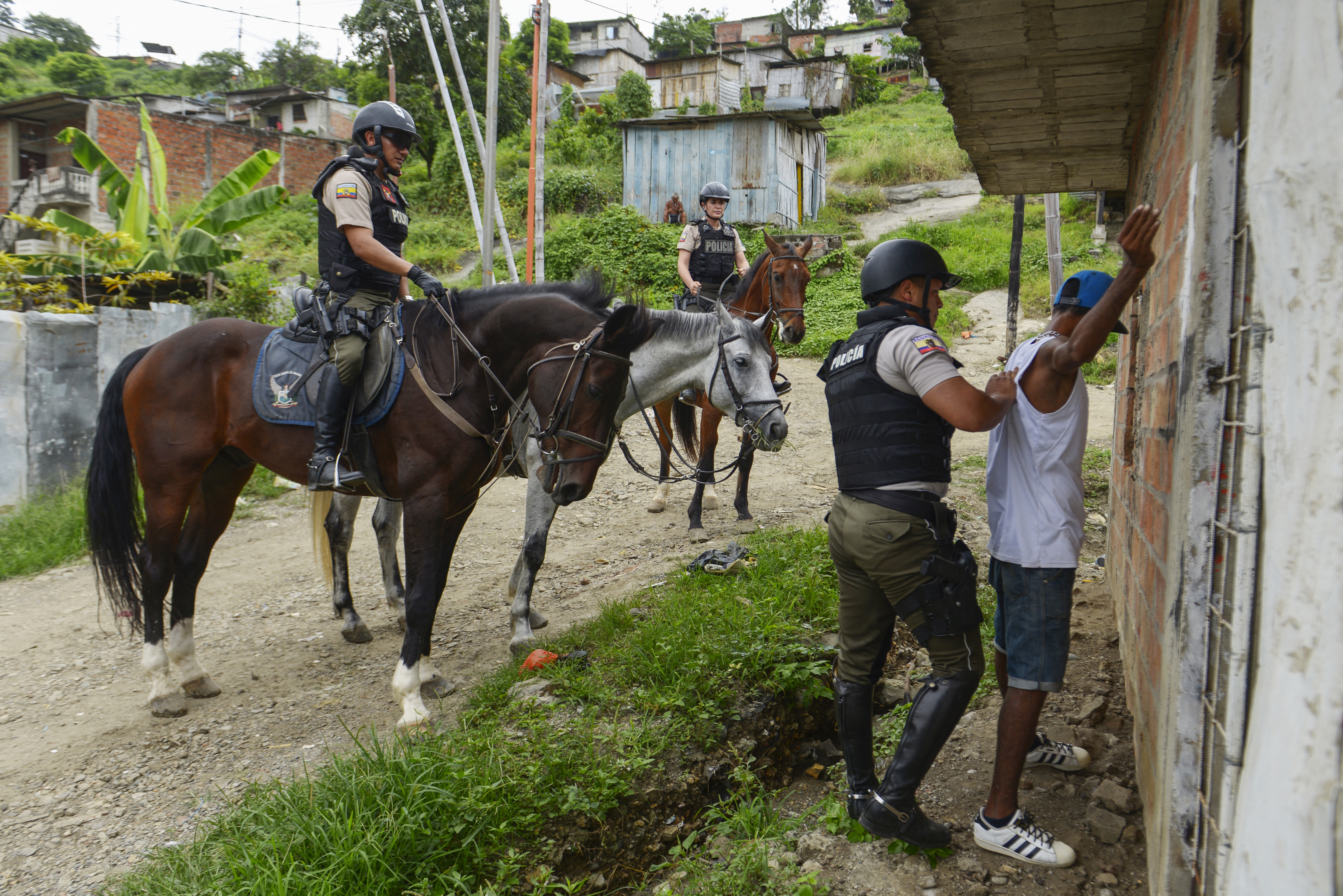 A mounted police officer frisks a man during a patrol in Cerro Las Cabras, Duran municipality, Ecuador, on April 26, 2022. - Drug traffickers have long targeted this hilly area to groom young recruits at their "school of assasins," a retired police chief told AFP under condition of anonymity. (Photo by Marcos PIN / AFP)