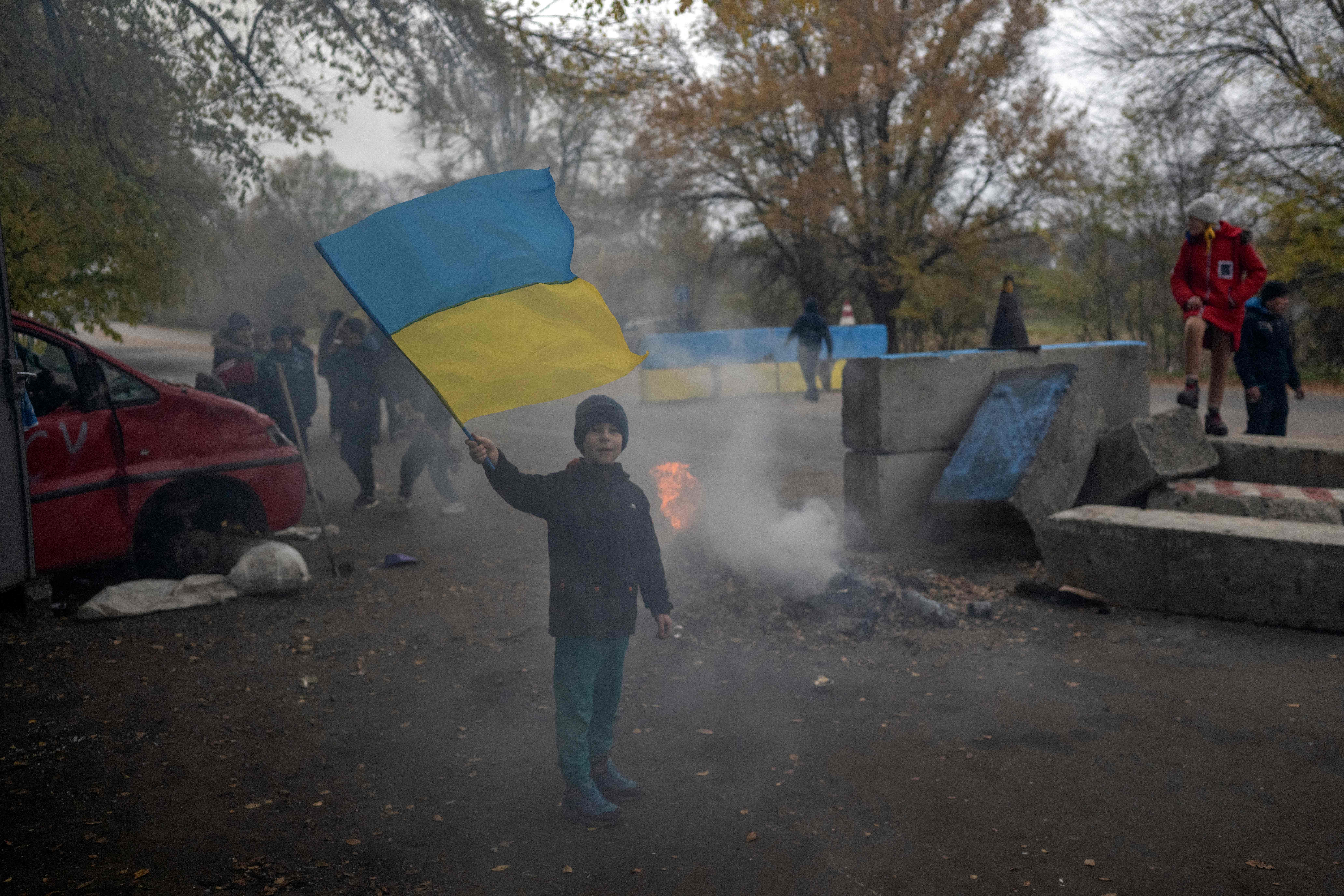 TOPSHOT - A young boy waves a Ukrainian flag at a former Russian checkpoint at the entrance of Kherson as local residents celebrate the liberation of the city, on November 13, 2022, amid Russia's invasion of Ukraine. - Ukrainians in the liberated southern city of Kherson expressed a sense of relief on November 11, 2022, after months of Russian occupation. There were no scenes of jubilation on November 13, 2022, an AFP correspondent said, but many locals said they felt a great sense of relief after Kyiv had wrested back control of the city. (Photo by AFP)