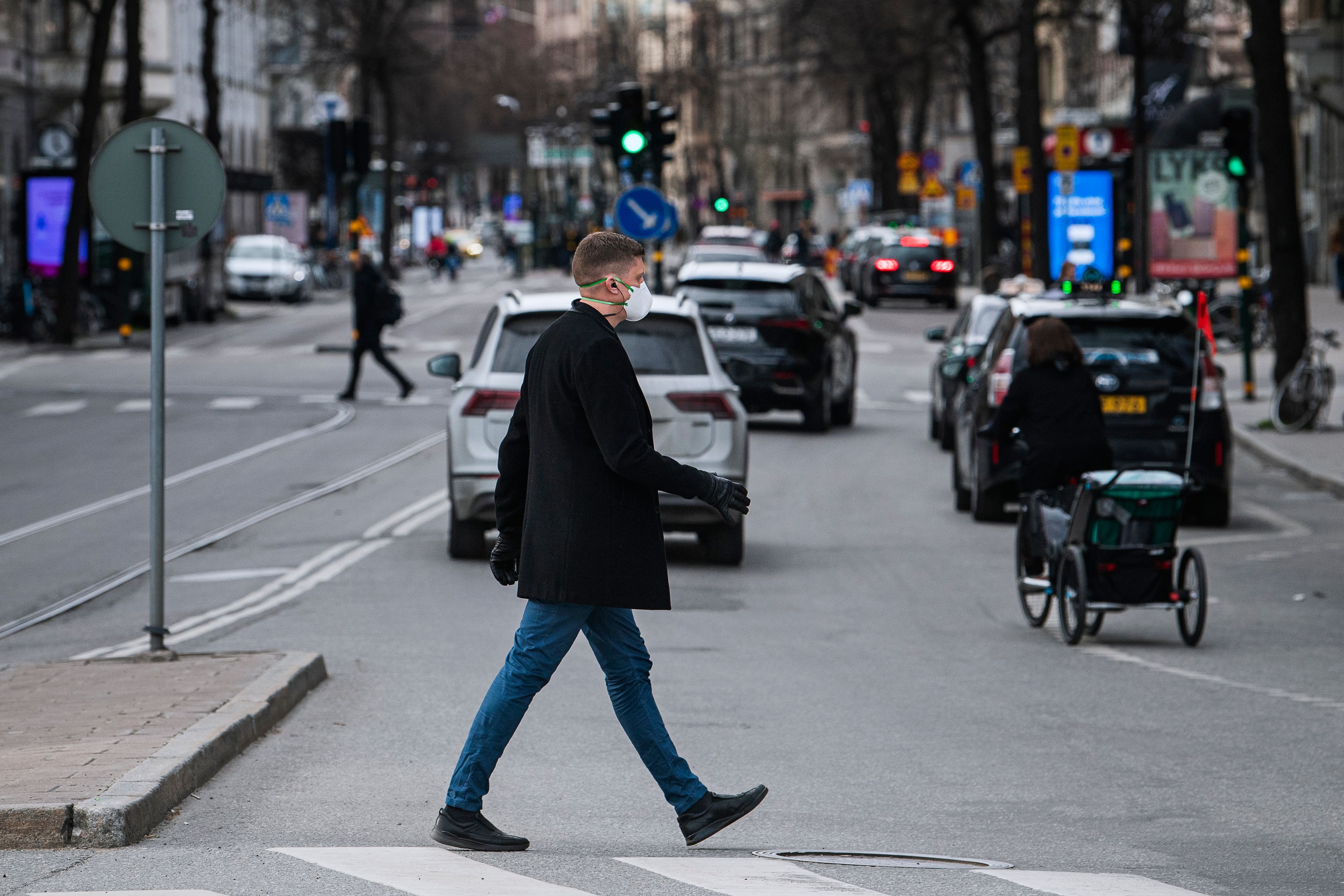 A pedestrian wearing a protective face mask crosses a busy street on April 16, 2020 in Stockholm, during the coronavirus COVID-19 pandemic. - Sweden's parliament passed a new law granting the government temporary powers to quickly adopt measures aimed at curbing the spread of the new coronavirus without prior parliamentary approval. (Photo by Jonathan NACKSTRAND / AFP)
