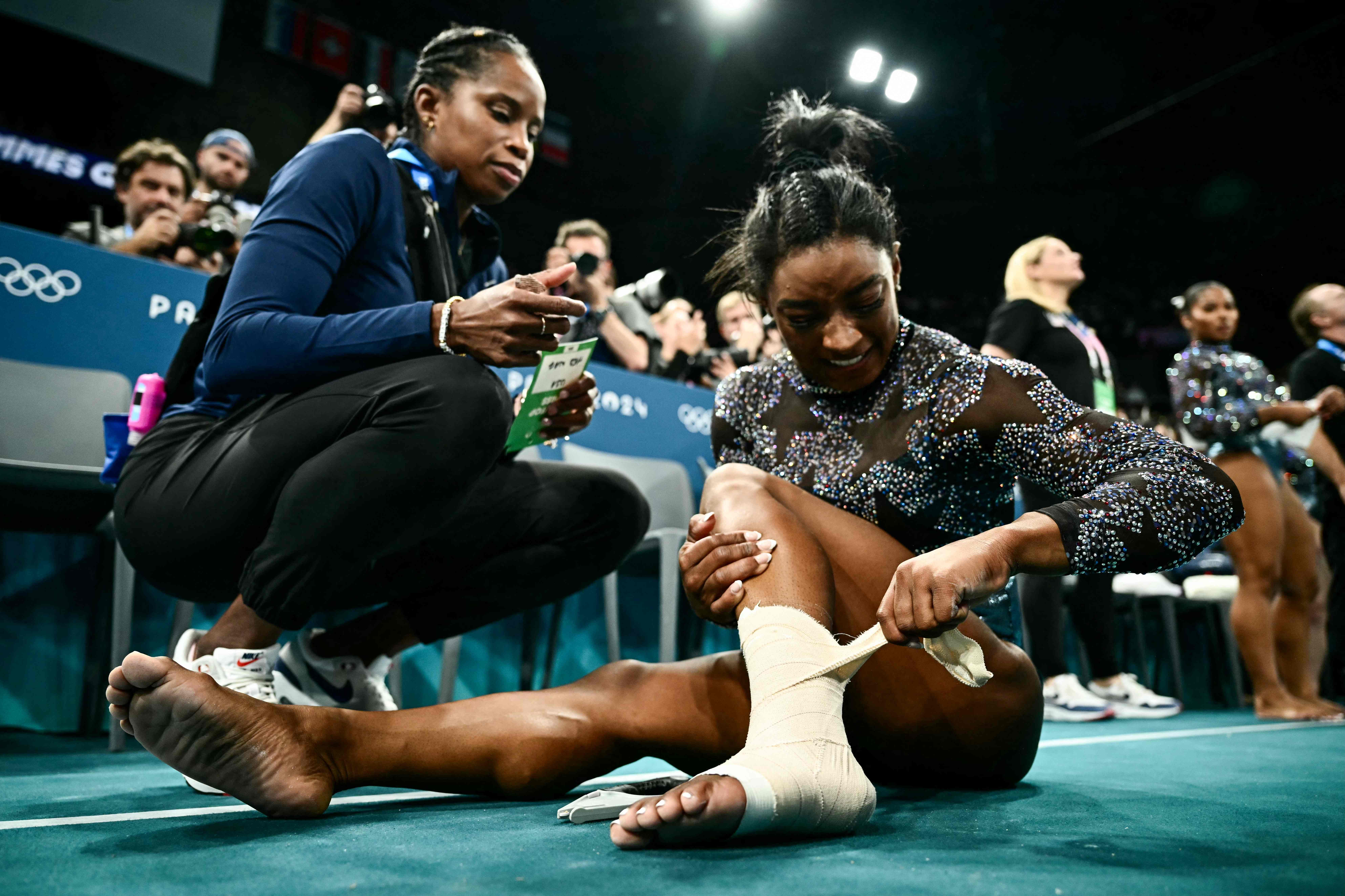 US' Simone Biles puts a strap on her left ankle during the artistic gymnastics women's qualification during the Paris 2024 Olympic Games at the Bercy Arena in Paris, on July 28, 2024. (Photo by Loic VENANCE / AFP)