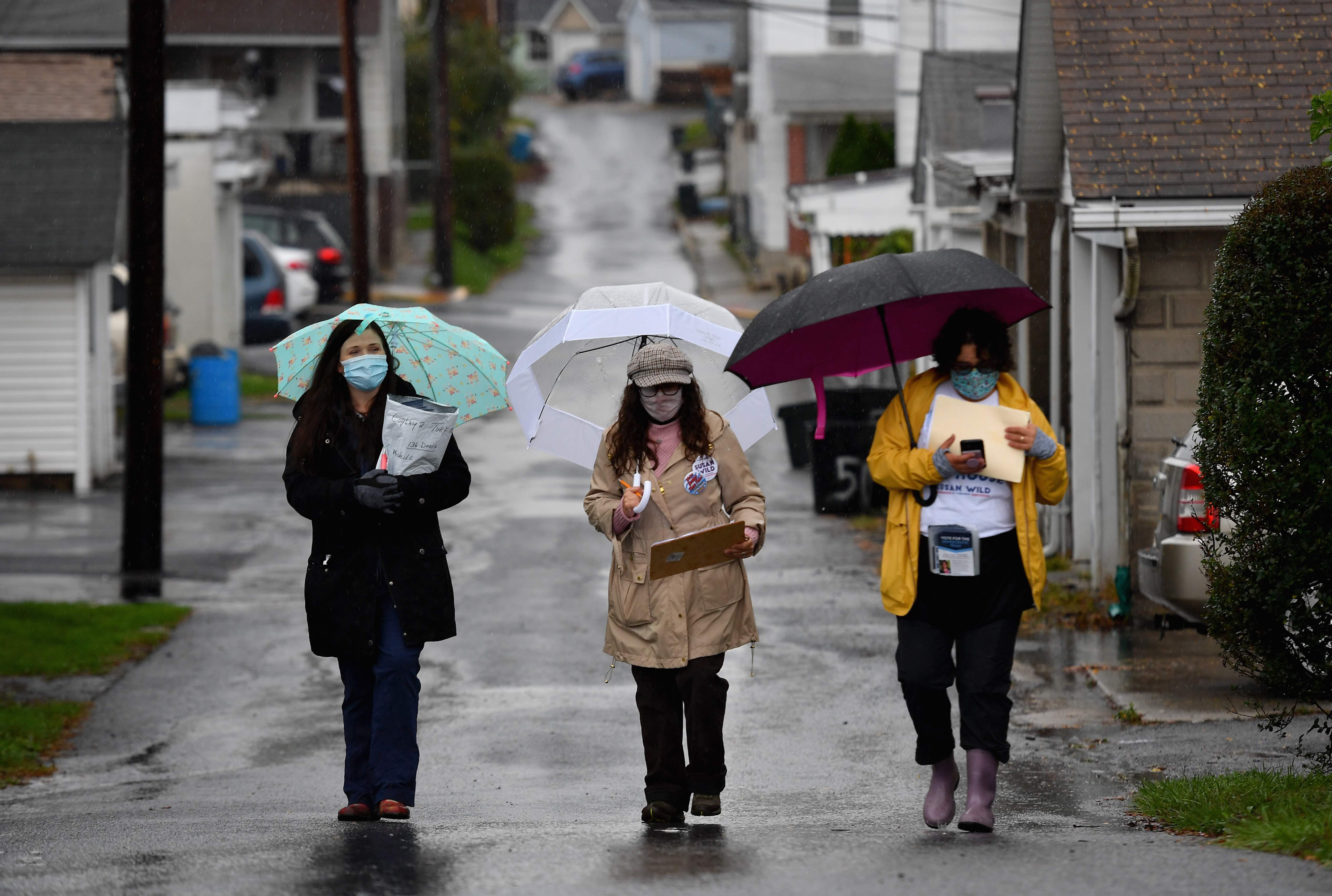 Democratic Party activists (L-R) Jamie Saye, Juniper Leifer, Heather Lipkin walk through a neighborhood after distributing information pamphlets to residents in Coplay, Pennsylvania on October 29, 2020. - In Pennsylvania, dedicated Democrats endure brush-offs from Republicans, shrugs of indifference from non-voters and householders wary of coronavirus as they make a final push for votes in a battleground state that could secure Joe Biden the presidency. "It's crunch time. We're pulling out all the stops," says 43-year-old Juniper Leifer, braving torrential rain, along with two other activists as they frantically knock on doors in an 11th-hour bid to win over any last-remaining undecided voters. (Photo by Angela Weiss / AFP)