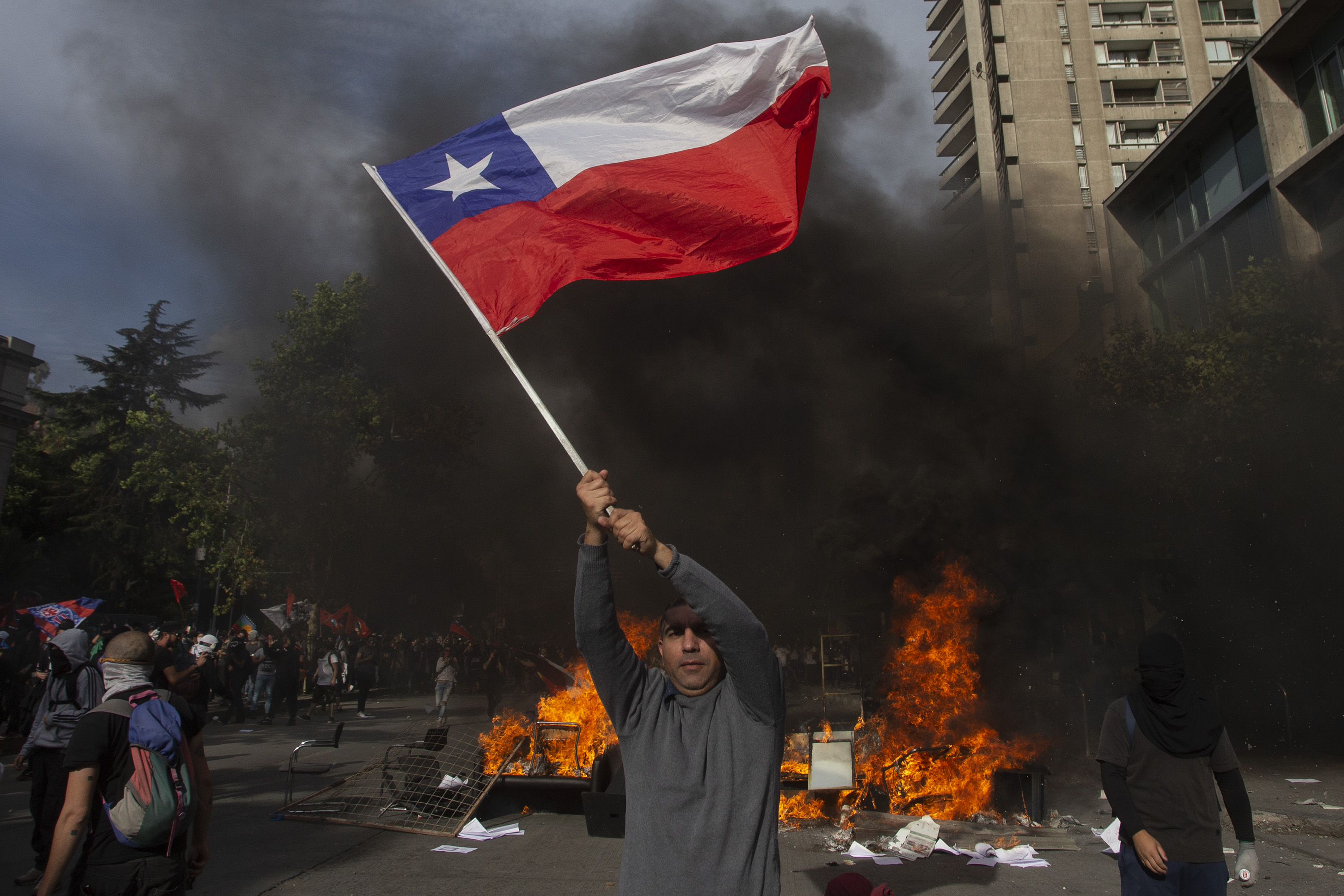 A demonstrator flutters a Chilean national flag at a barricade during a protest against the government's economic policies in Santiago on October 29, 2019. - Chilean President Sebastian Pinera unveiled a major cabinet reshuffle on the eve as he battles to find a response to more than a week of street protests that have left at least 20 people dead. Protesters have been demanding Pinera's resignation and despite his making a raft of concessions including an increase in the minimum wage and pensions, public unrest shows no sign of abating. (Photo by CLAUDIO REYES / AFP)