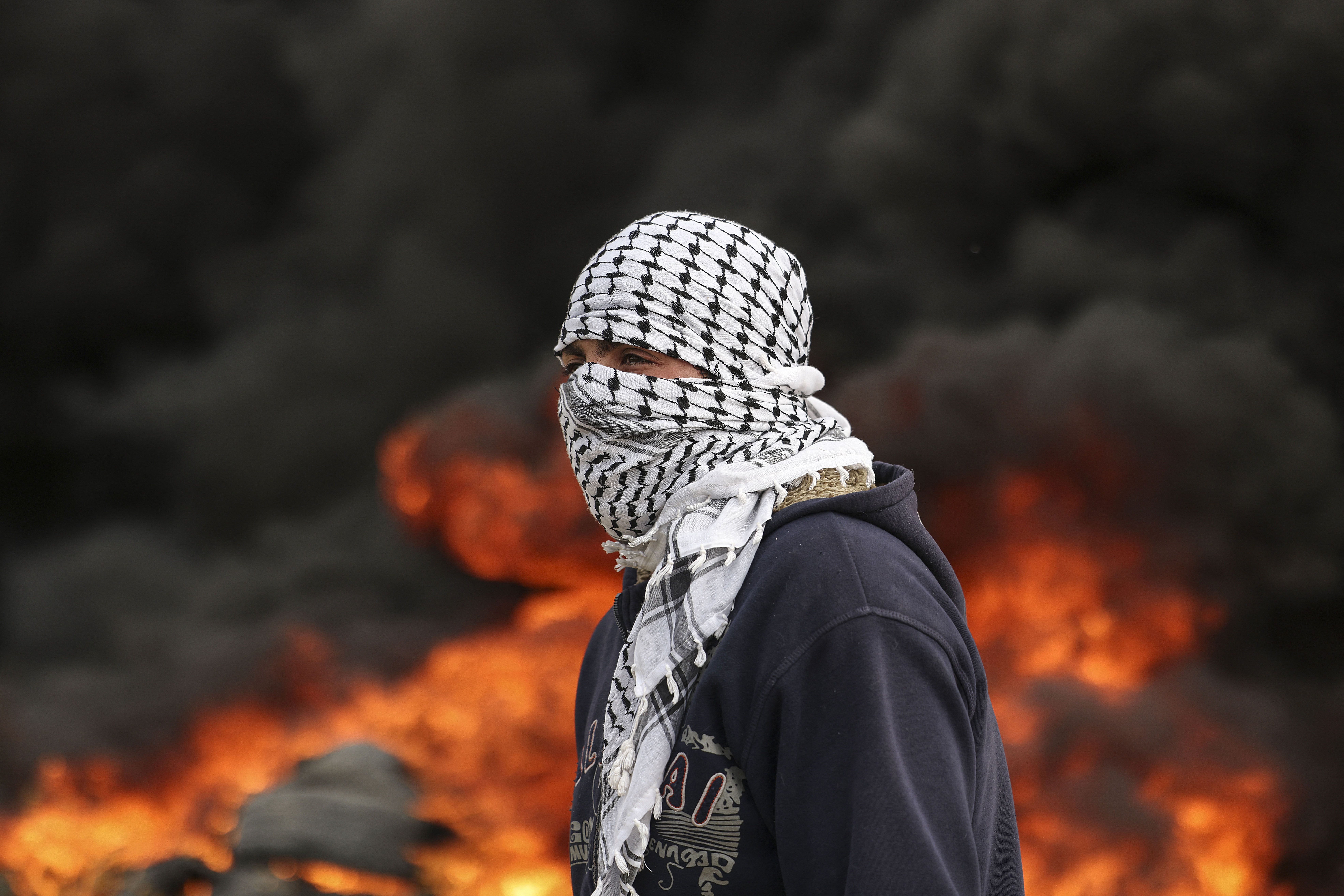 A masked Palestinian youth stands near burning tires during a protest near the Israel-Gaza border east of Jabalia refugee camp, on February 23, 2023. - Israel and Palestinian militants traded air strikes and rocket fire in and around Gaza, a day after the deadliest Israeli army raid in the occupied West Bank in nearly 20 years. (Photo by Mahmud HAMS / AFP)