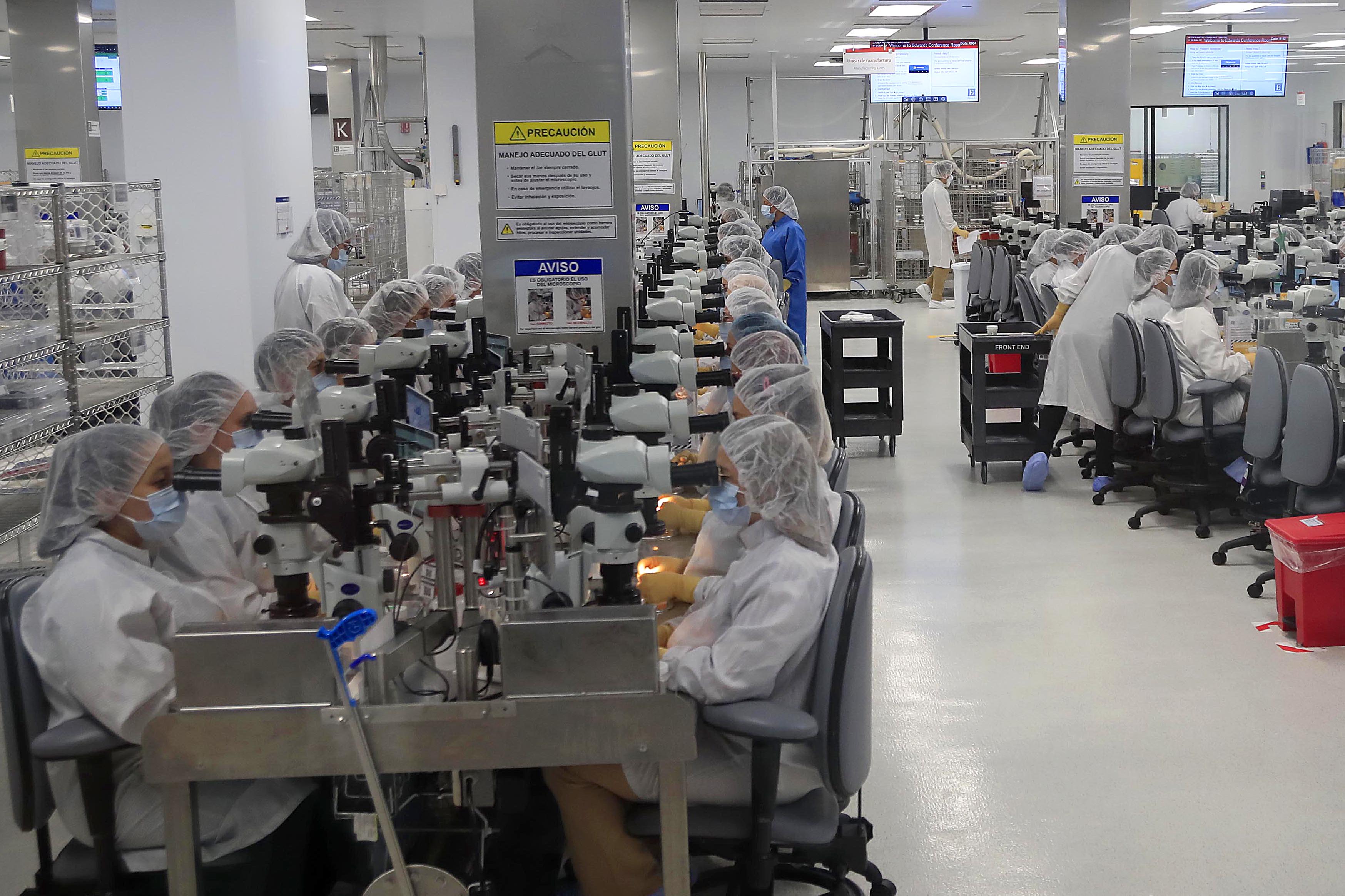 Personas trabajando en un centro de manufactura de Edwards Lifesciences en Cartago, utilizando microscopios y vestimenta de laboratorio en un espacio limpio y organizado.