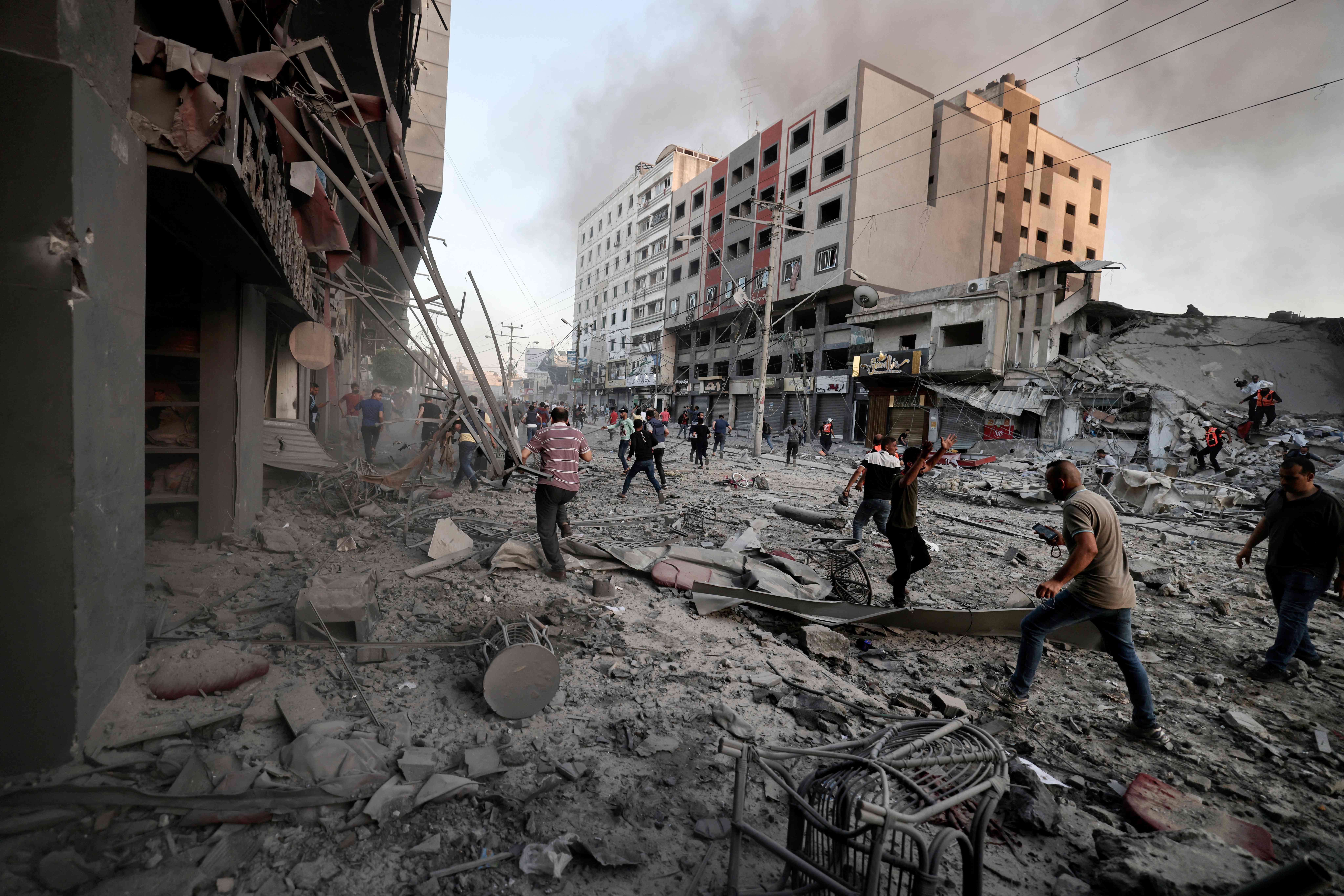 People gather amidst the rubble in front of Al-Sharouk tower that collapses after being hit by an Israeli air strike, in Gaza City, on May 12, 2021. - An Israeli air strike destroyed a multi-storey building in Gaza City today, AFP reporters said, as the Jewish state continued its heavy bombardment of the Palestinian enclave. (Photo by Mohammed ABED / AFP)