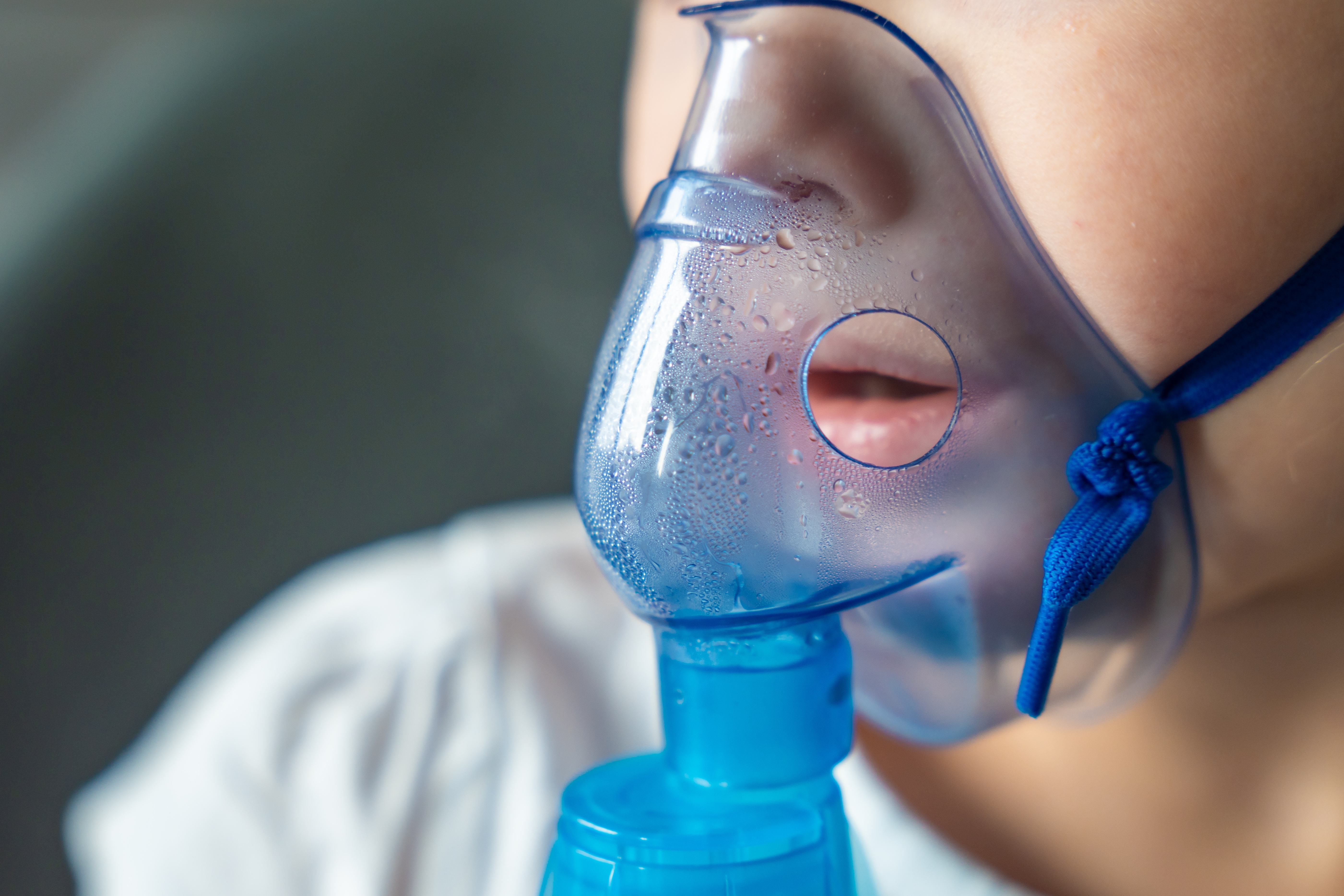 Primer plano de cara de niño/niña con mascarilla de nebulización/nebulizaciones por asma u otras afecciones respiratorias