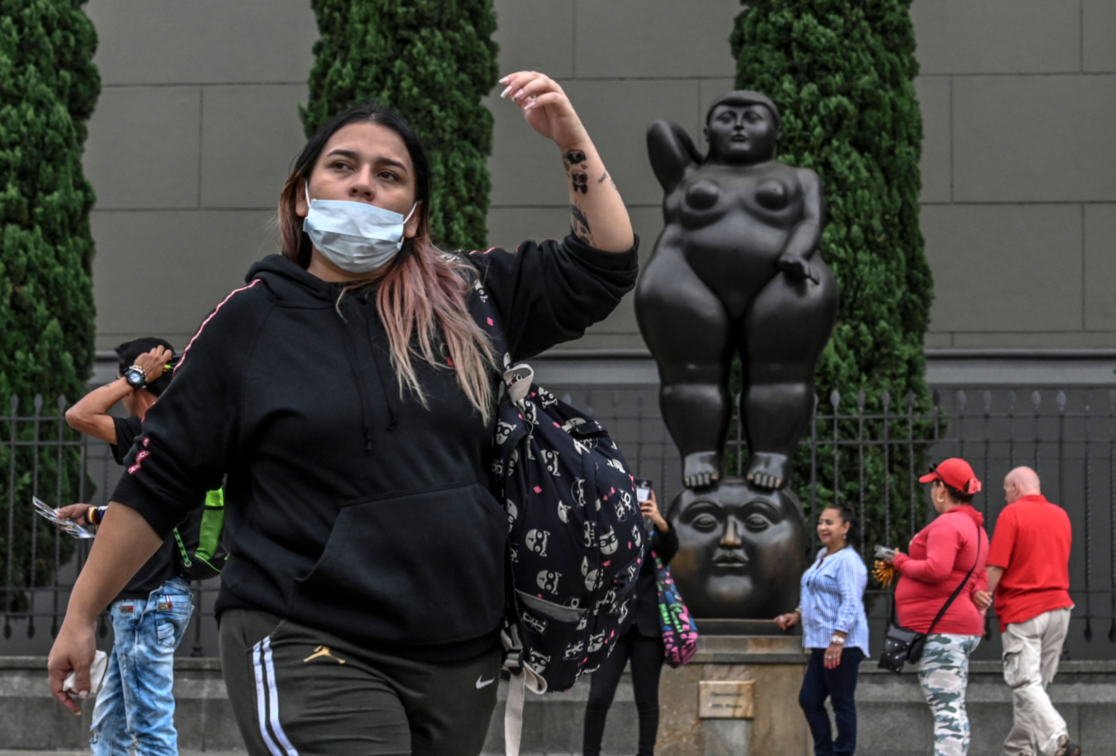 A woman wears a protective face mask as a preventive measure against the spread of the new Coronavirus, COVID-19, near a statue by Colombian sculptor Fernando Botero, in Medellin, Colombia on March 11, 2020. - The World Health Organisation (WHO) declared the Coronavirus a pandemic with 118,000 cases in about 120 countries, and 4000 deaths. (Photo by JOAQUIN SARMIENTO / AFP)