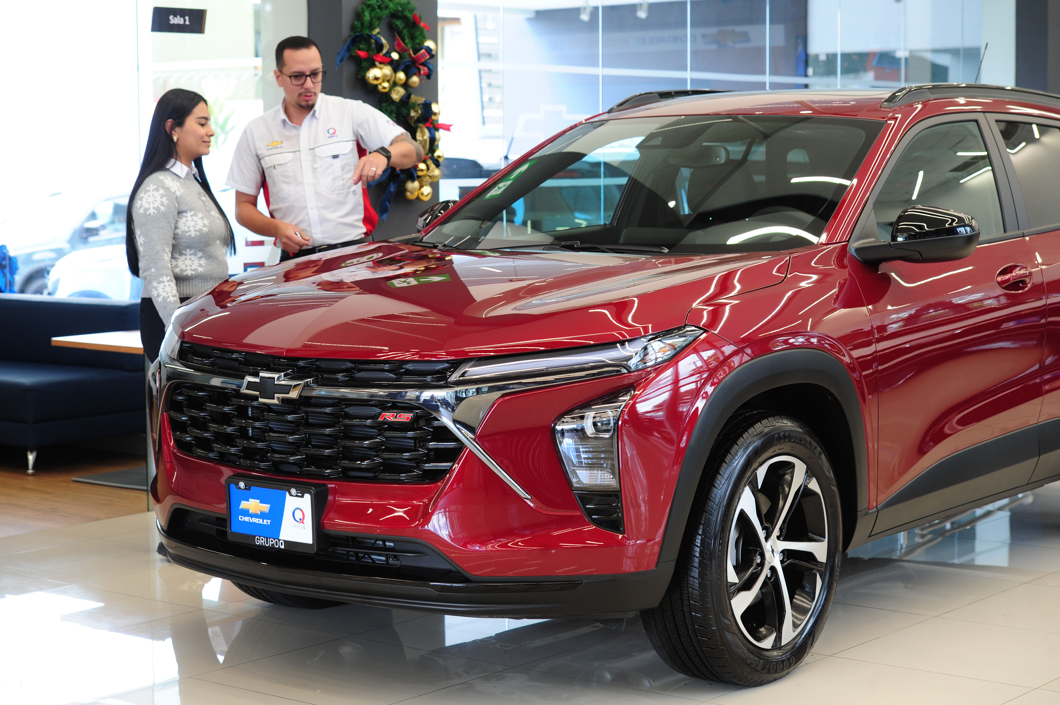 Asesor automotriz mostrando un Chevrolet rojo a una clienta en concesionario, relacionado con el auge del crédito para vehículos en Costa Rica.