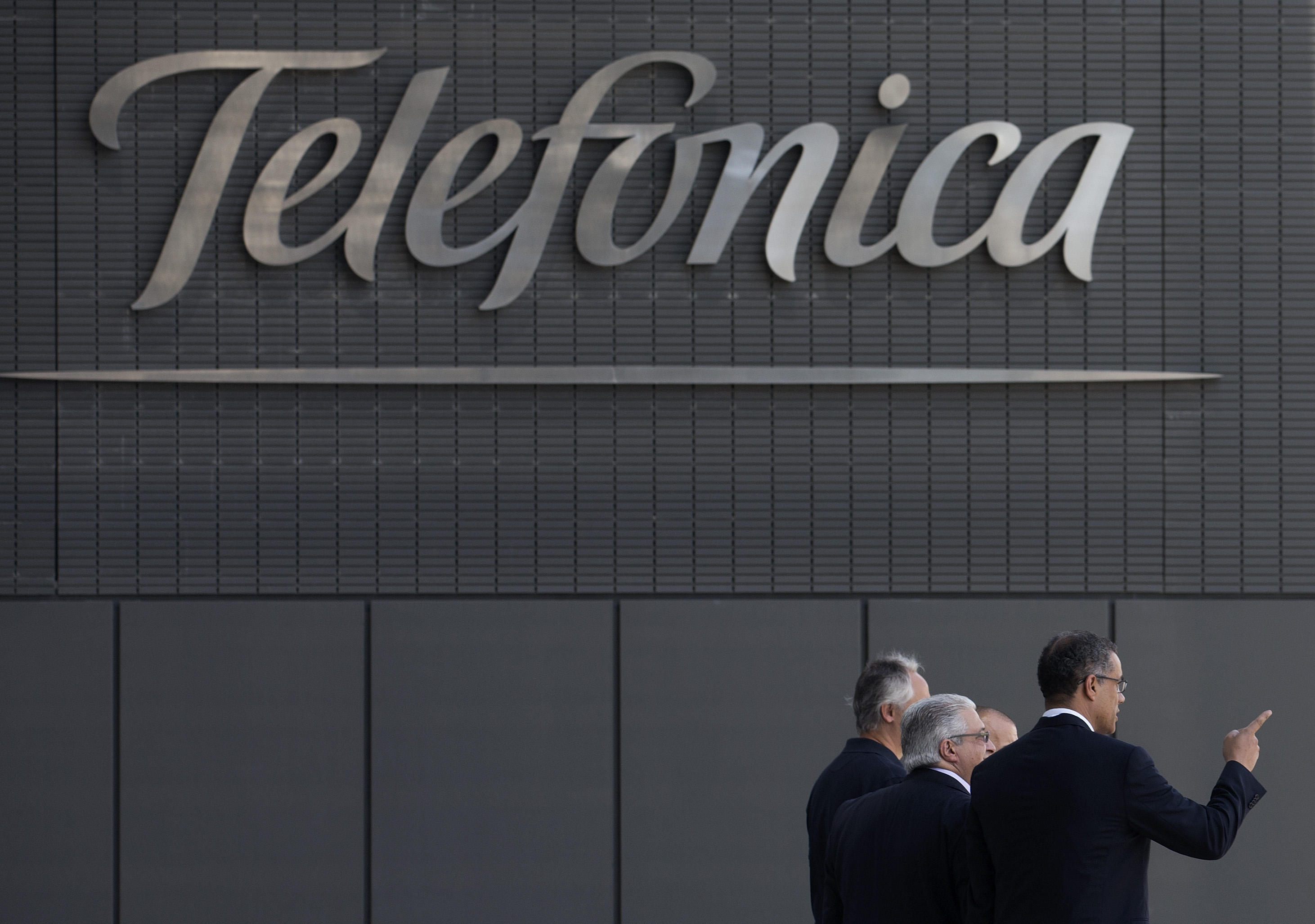 Men walk out of Telefonica head offices in Madrid, Tuesday July 23, 2013. Spain's Telefonica has agreed to buy German mobile unit E-Plus from Dutch telecommunications company Royal KPN NV for euro 5 billion ($6.58 billion) plus shares, a deal that would create Germany's biggest cellphone operator in terms of customers. The proposed deal announced Tuesday would bring together E-Plus, currently Germany's No. 3 operator with 23.4 million customers, with O2, the fourth-biggest, which is already owned by Telefonica and has 19.3 million customers. (AP Photo/Paul White)